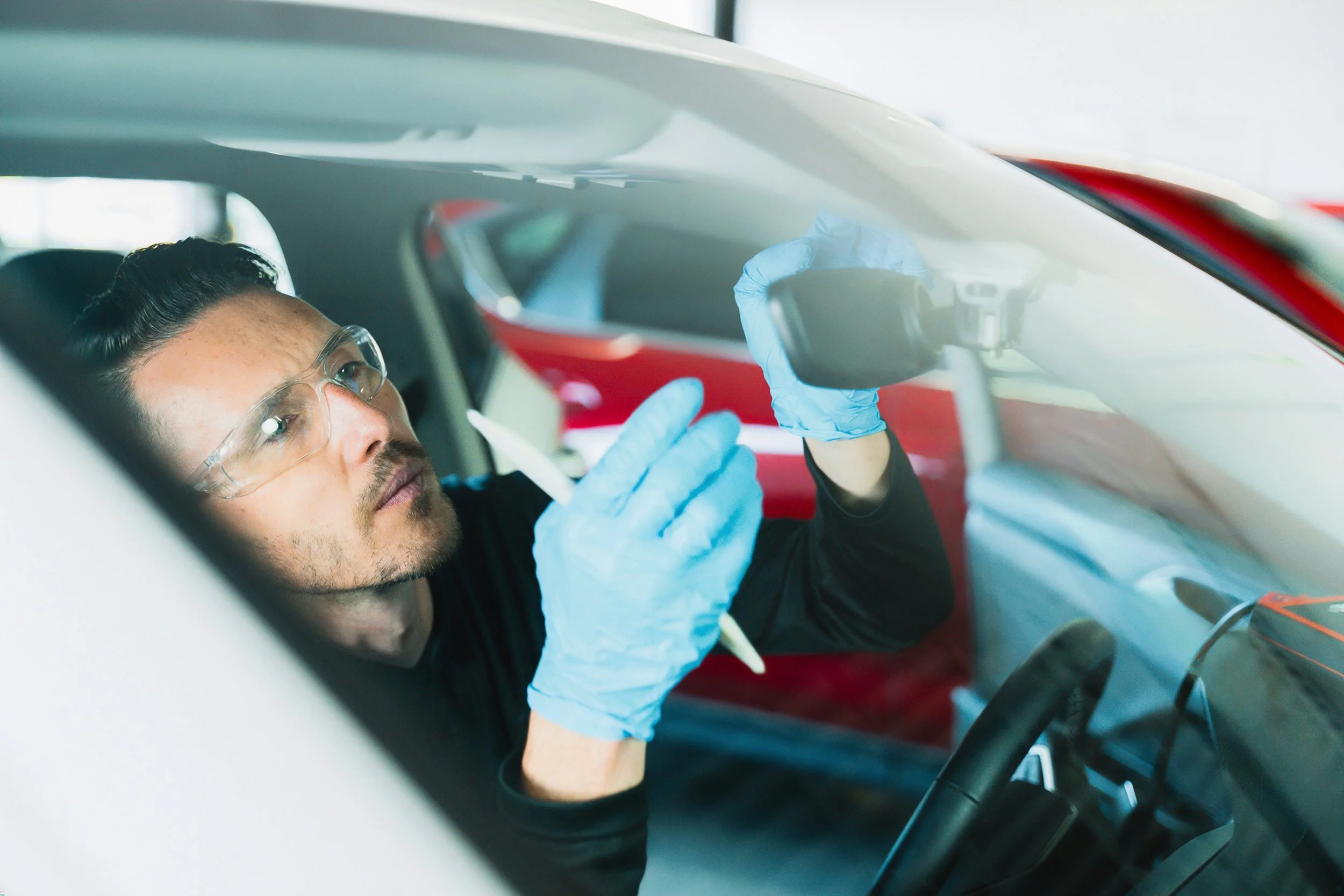 Technician in gloves fitting the mirror and camera housing on a windshield