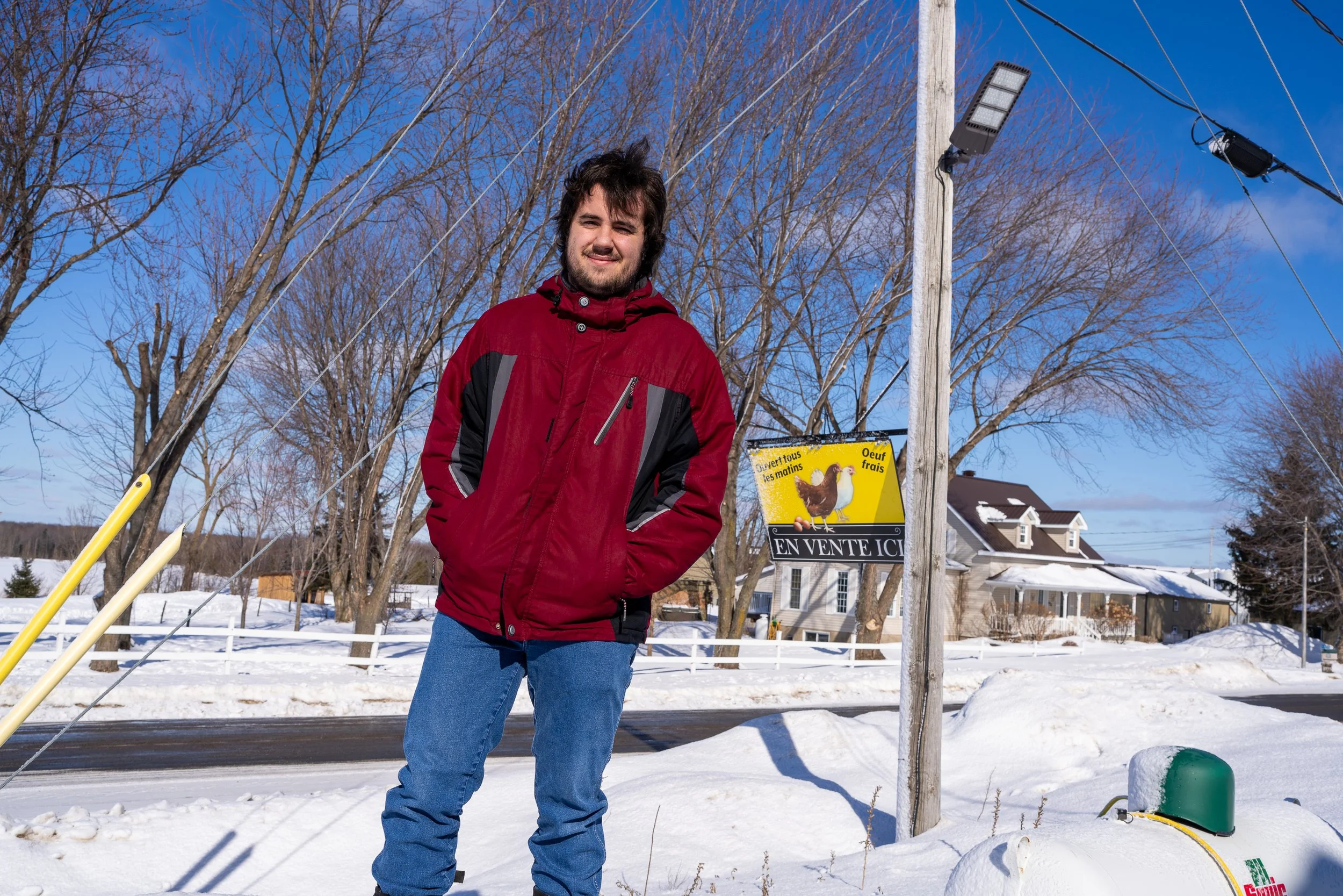 Young farmer in a red winter coat in front of the family farm sign