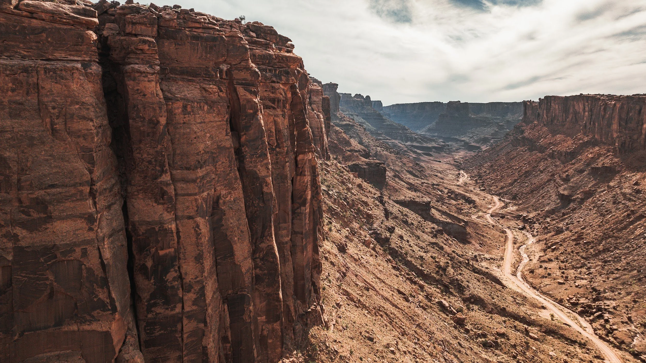 Aerial view of a dirt road winding along the bottom of a red rock canyon in Utah.