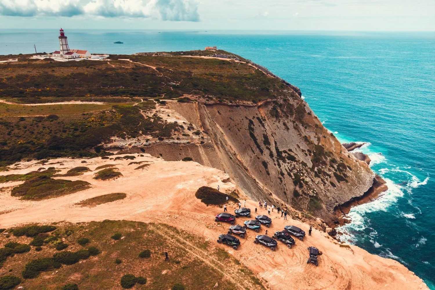 Aerial view of the 34° convoy parked on a clifftop beside a lighthouse on the Portuguese coast