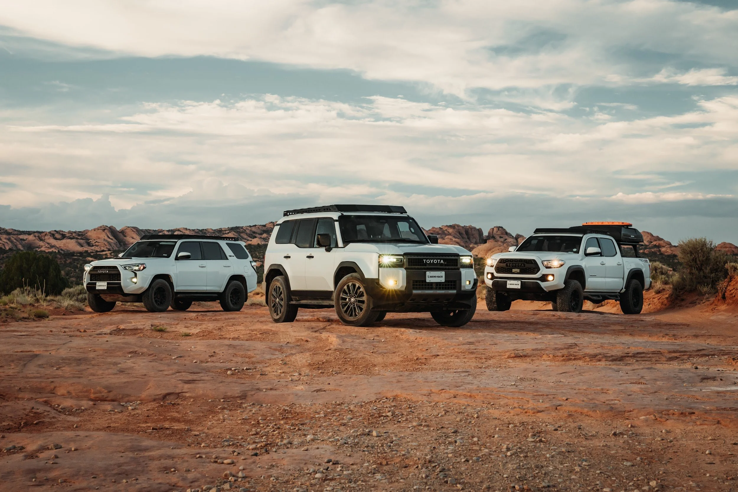 4Runner, Land Cruiser and Tacoma lined up on red dirt in Utah, each with a Rhino-Rack setup.