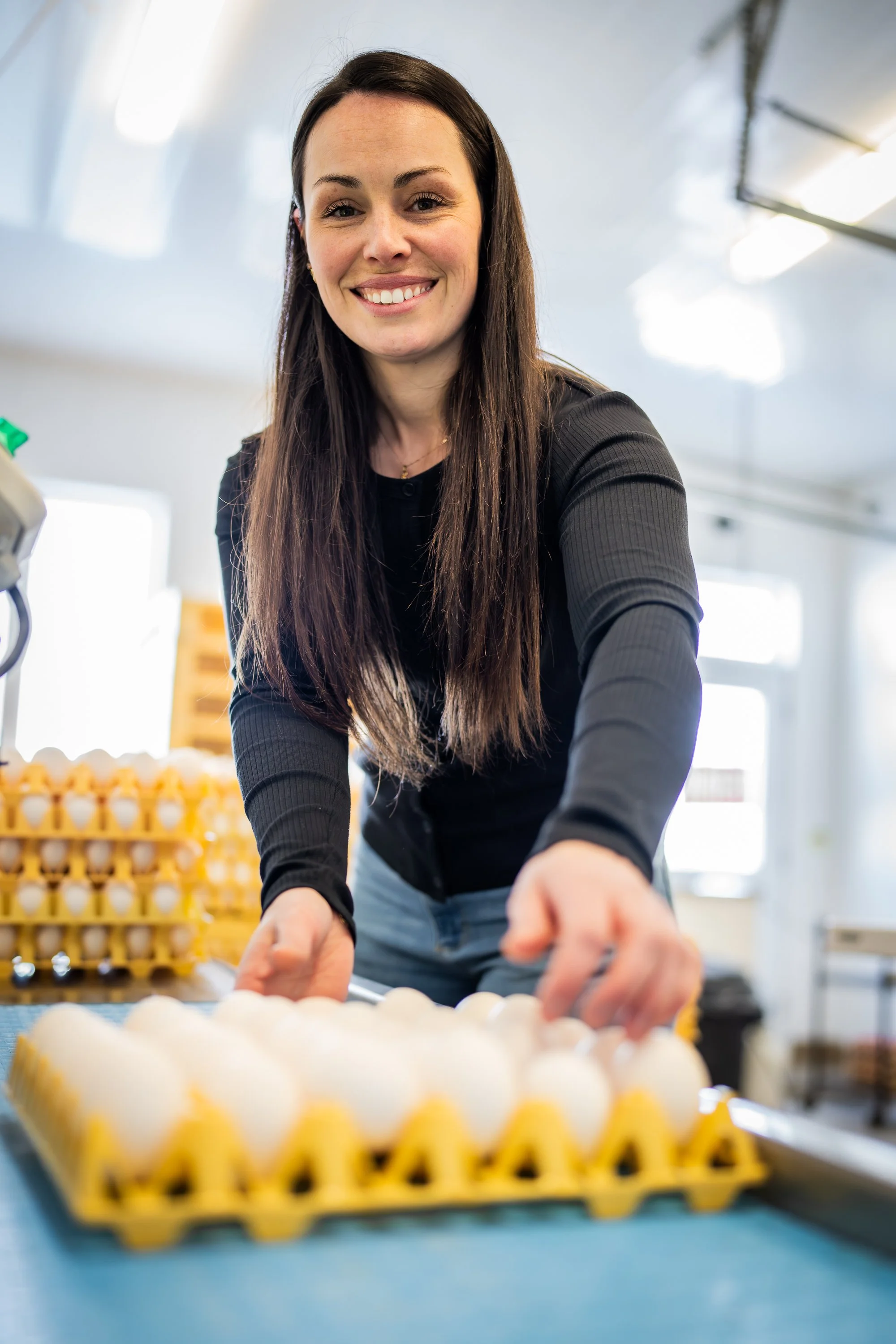 Farm worker smiling as she places eggs in a yellow tray