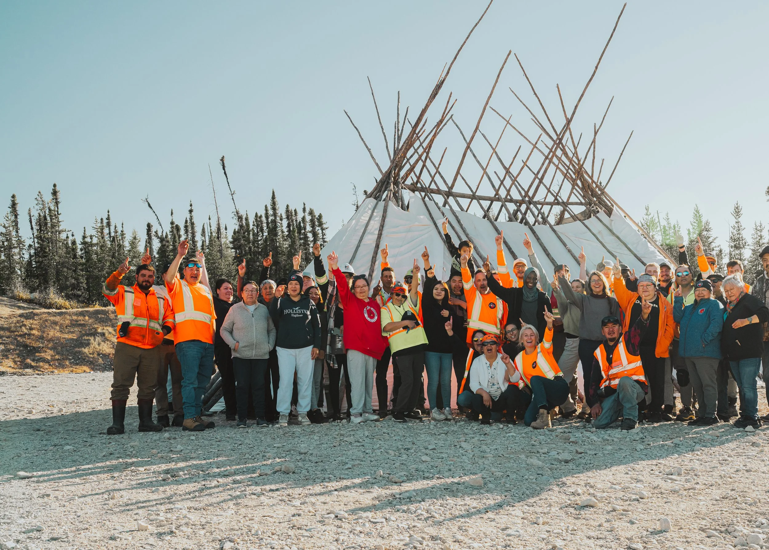 Large group of camp workers and community members waving in front of a tipi frame