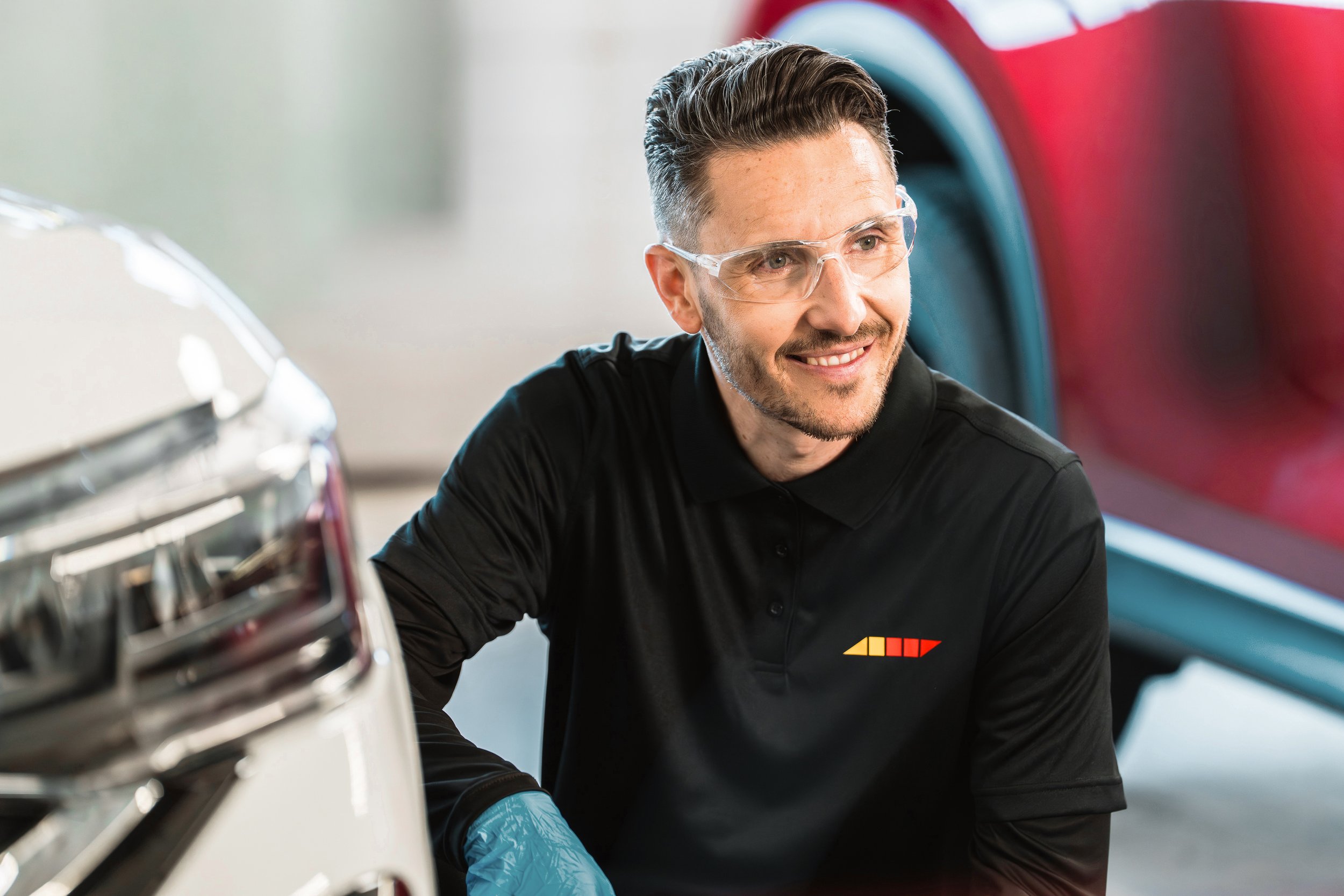 Lebeau technician in safety glasses smiling beside a headlight