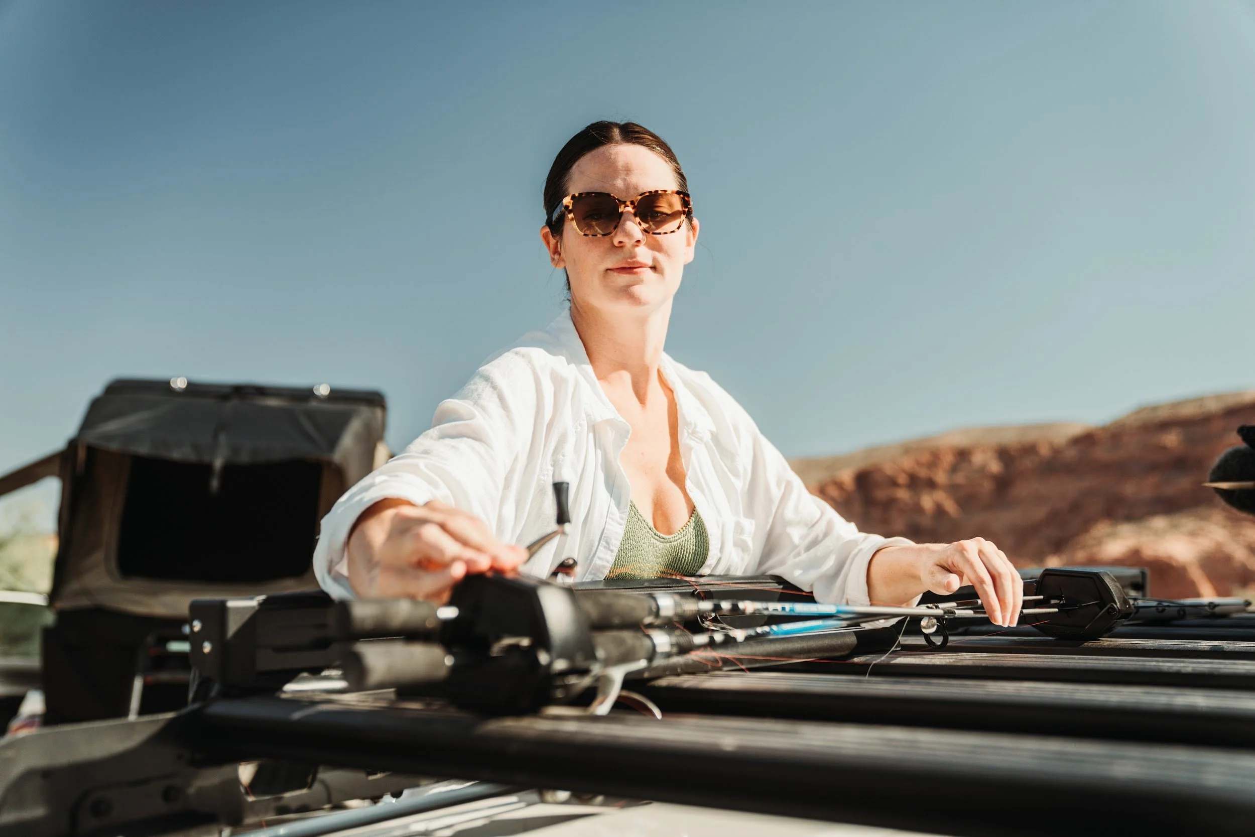 Woman loading fishing rods into a holder on the Rhino-Rack platform, red rock behind.