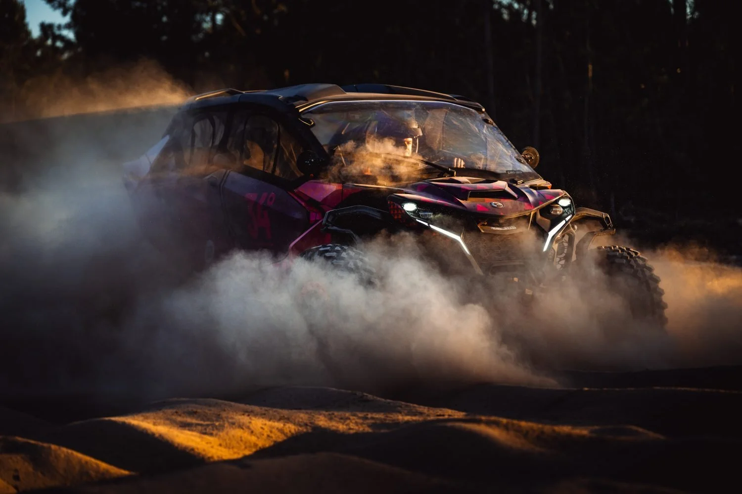 A 34° side-by-side in a cloud of dust at dusk, headlights on