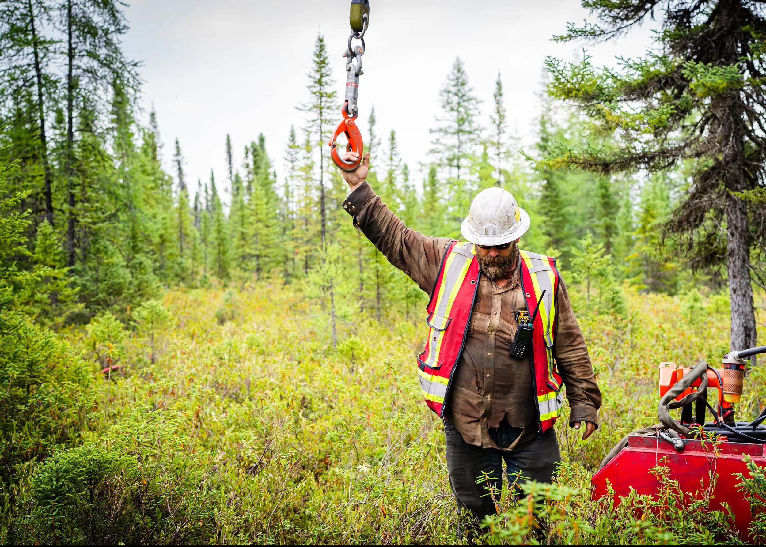 Worker in a hard hat reaching up to a helicopter sling hook in the bush