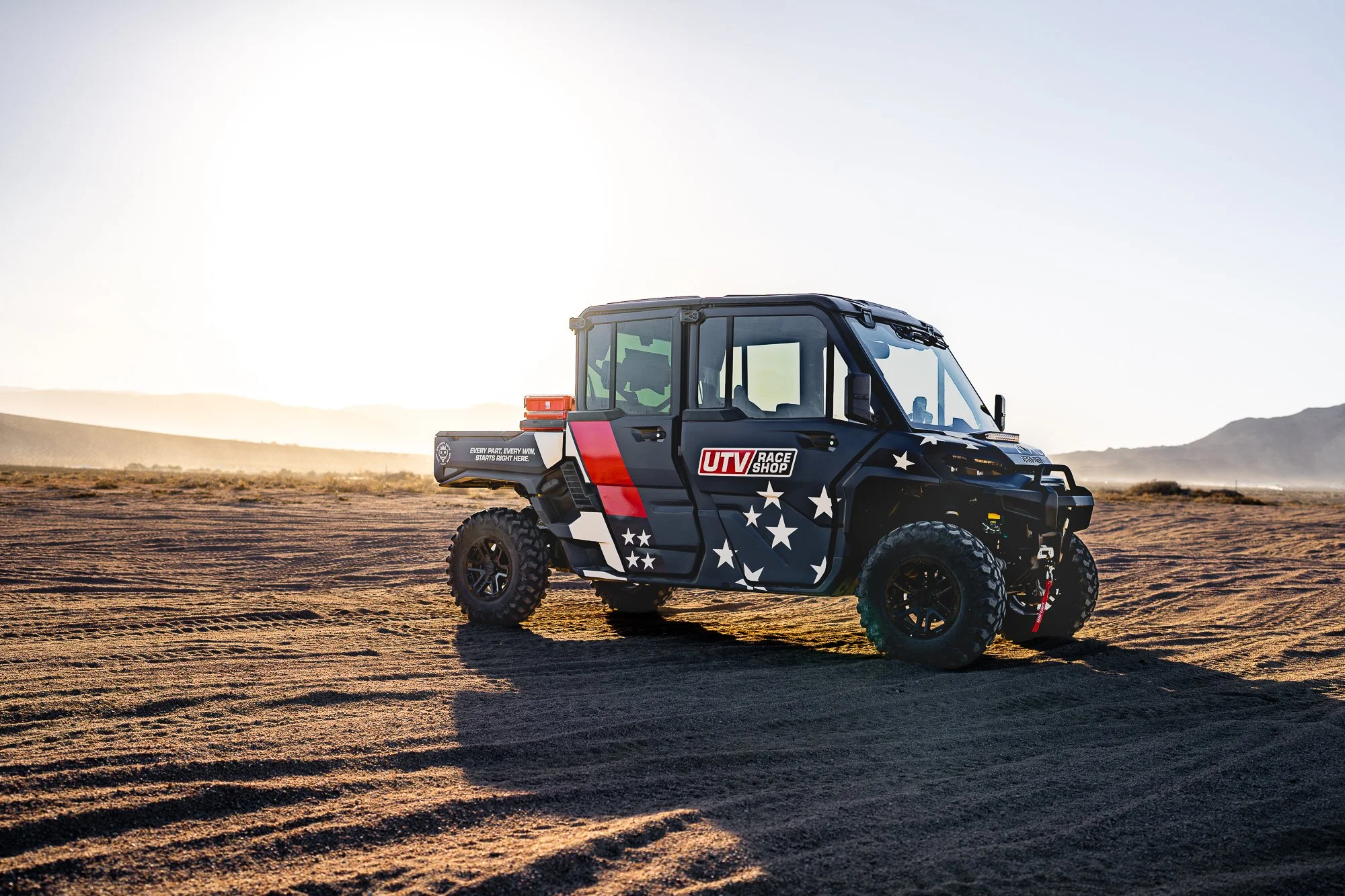 A Can-Am Defender wrapped in the new UTV Race Shop identity, navy with white stars and a red stripe, in the desert at King of the Hammers 2026.
