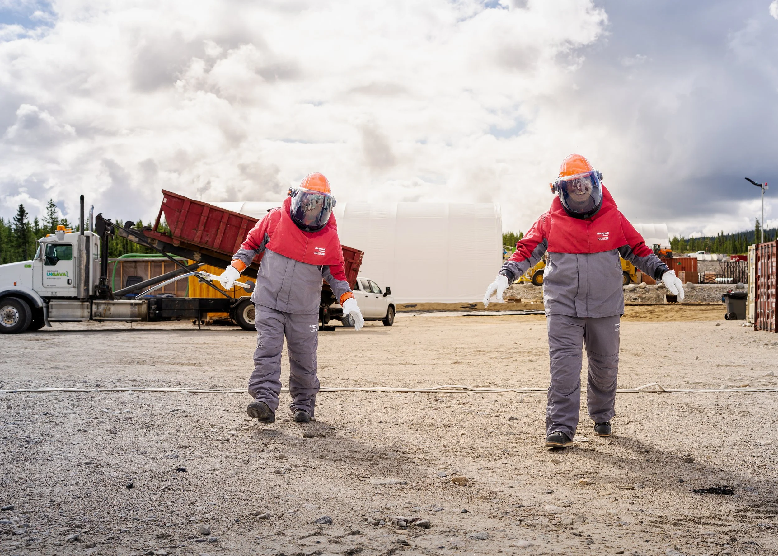Two workers in cold-weather gear and face shields walking across the camp yard