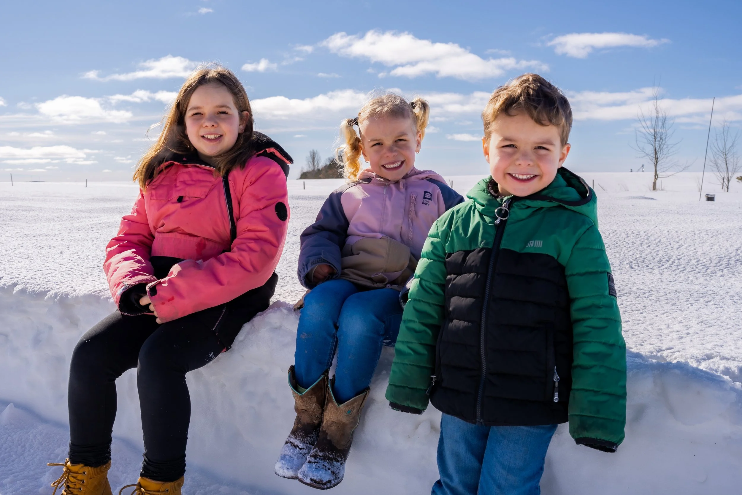 Three children in winter coats sitting on a snowbank