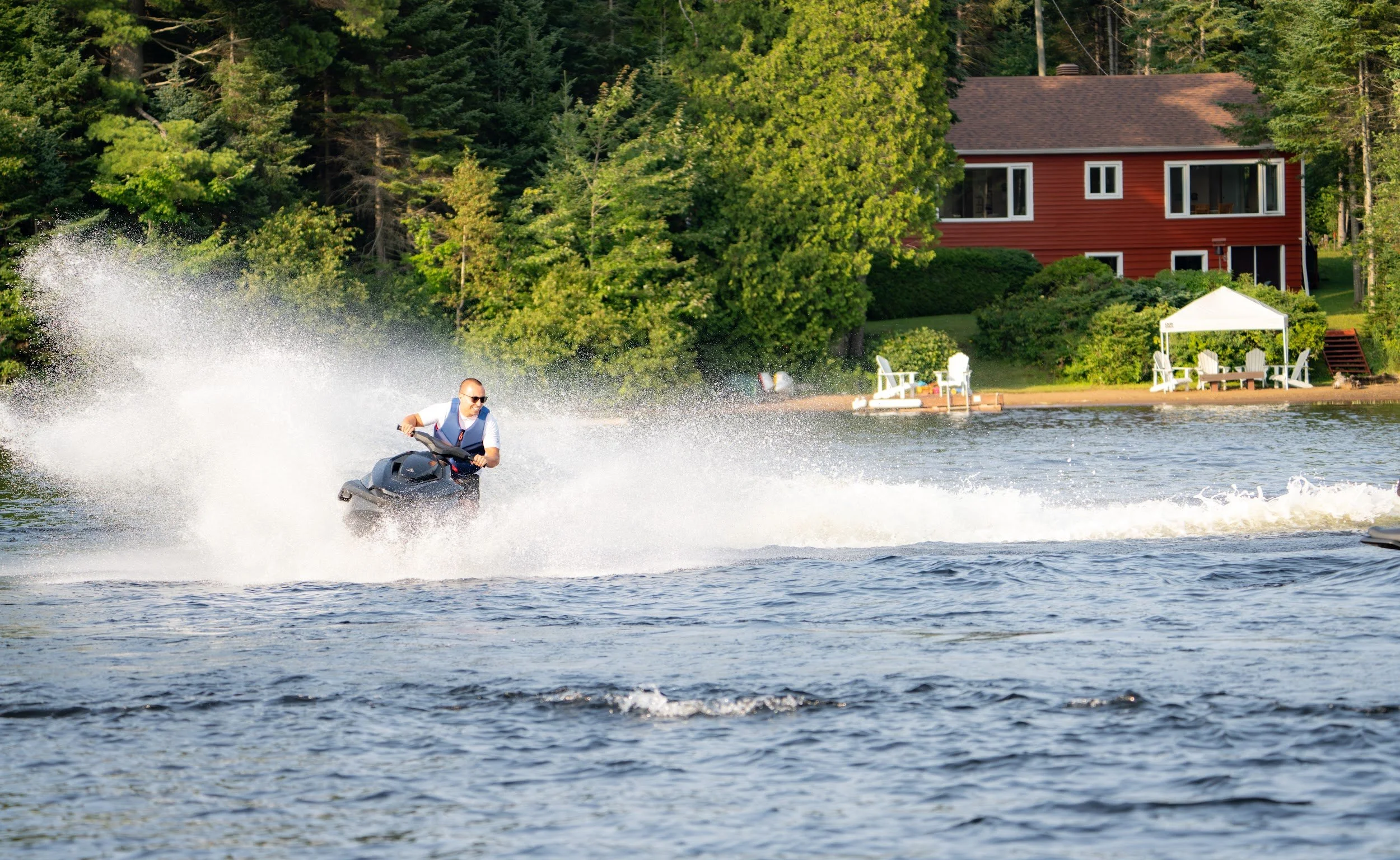 Rider on a Taiga Orca throwing a tall rooster tail of spray past a red cottage