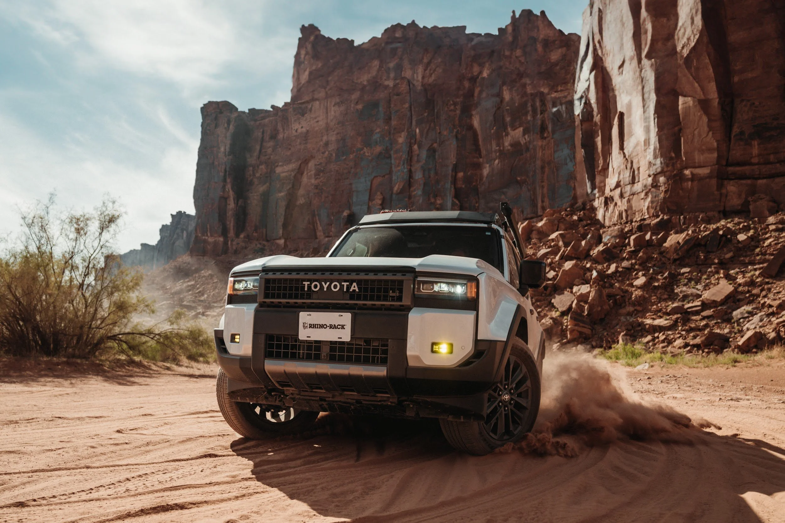 Land Cruiser kicking up sand below red sandstone cliffs in Utah.