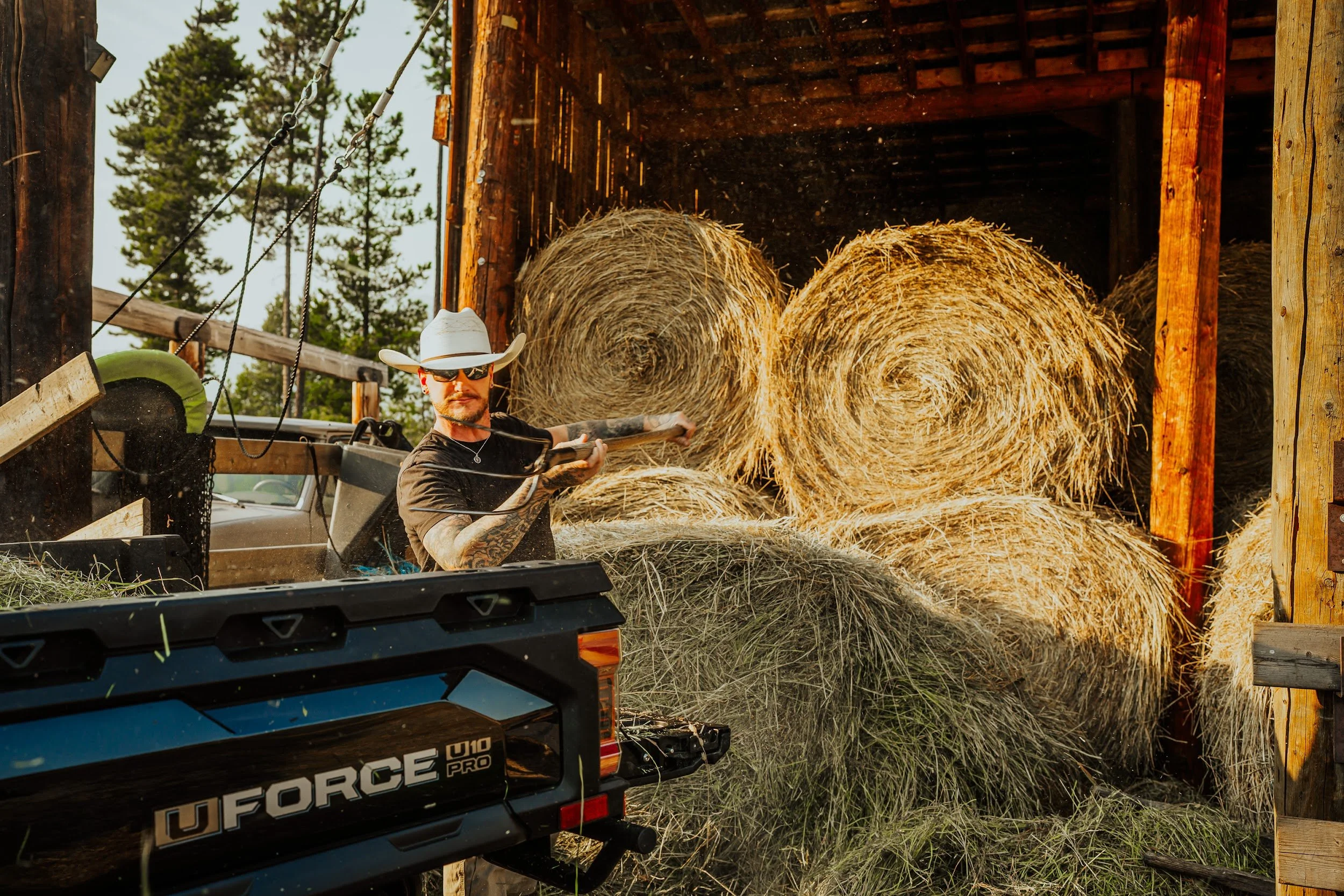 A rancher forks hay from the round bales into the bed of a CFMOTO UFORCE at the hay barn.