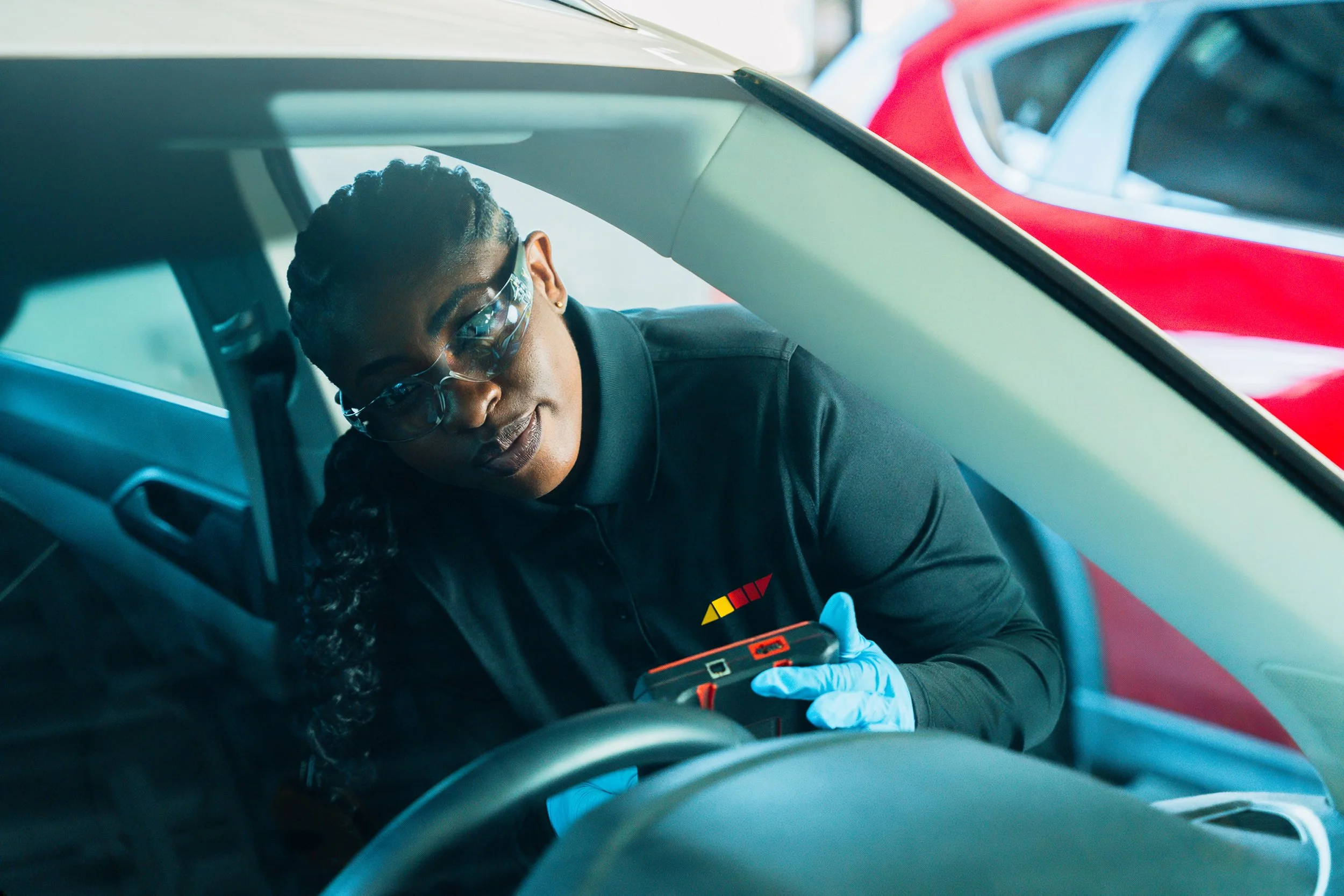 Technician in the driver's seat running an ADAS calibration with a handheld tool