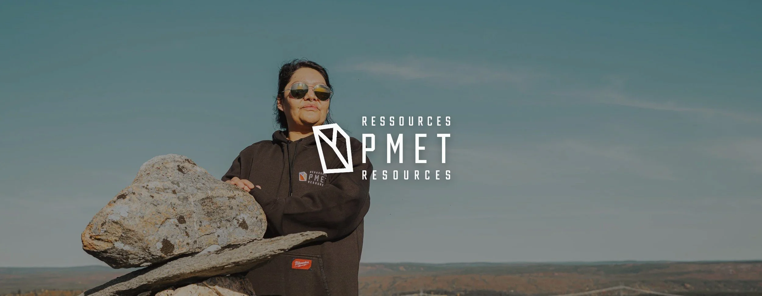 Femme près d'un inukshuk en pierre au-dessus de la taïga de la Baie-James, avec le logo de PMET Resources par-dessus la photo