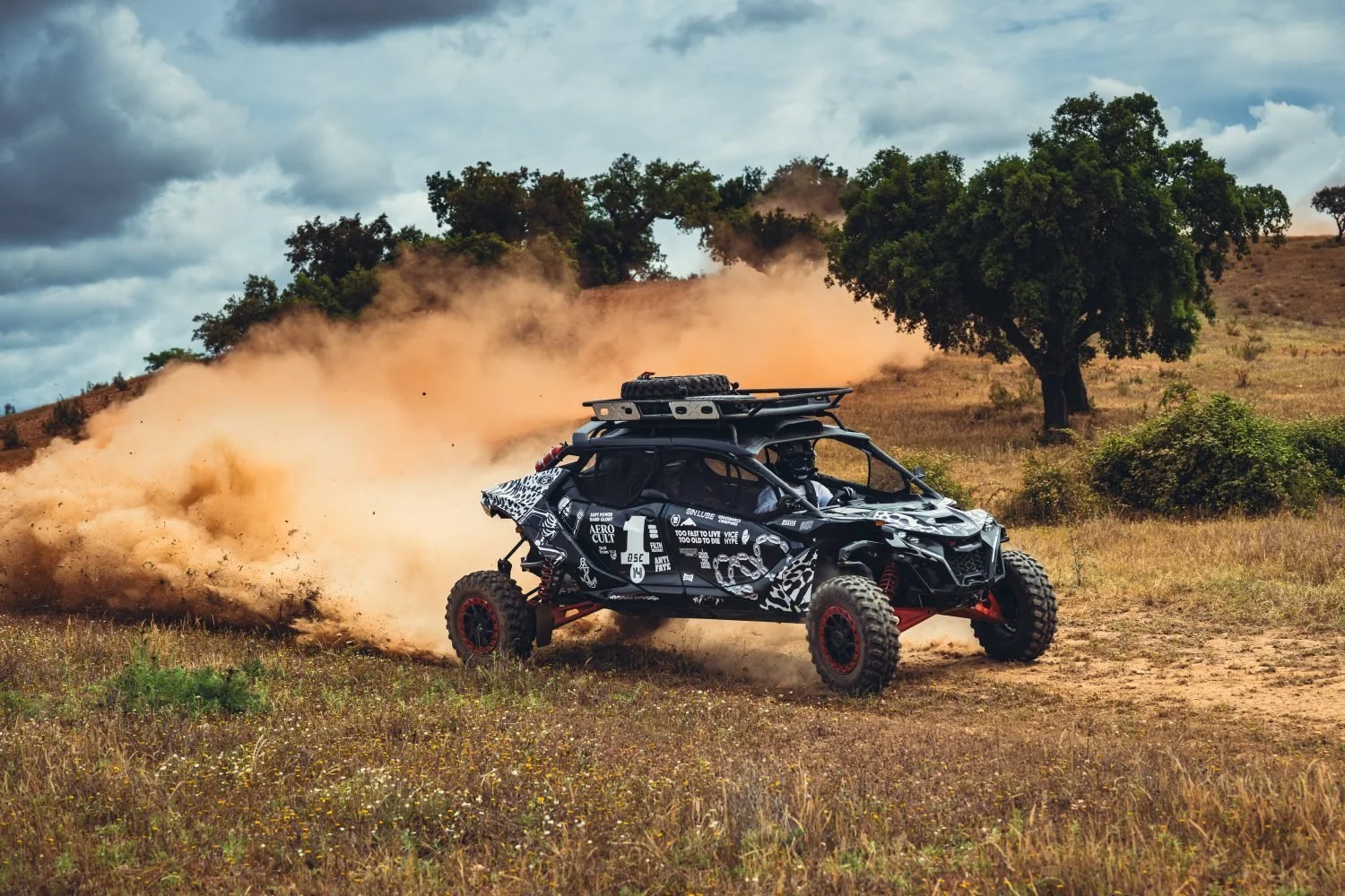 A patterned 34° side-by-side drifting through dry grass under cork oaks, dust trailing behind