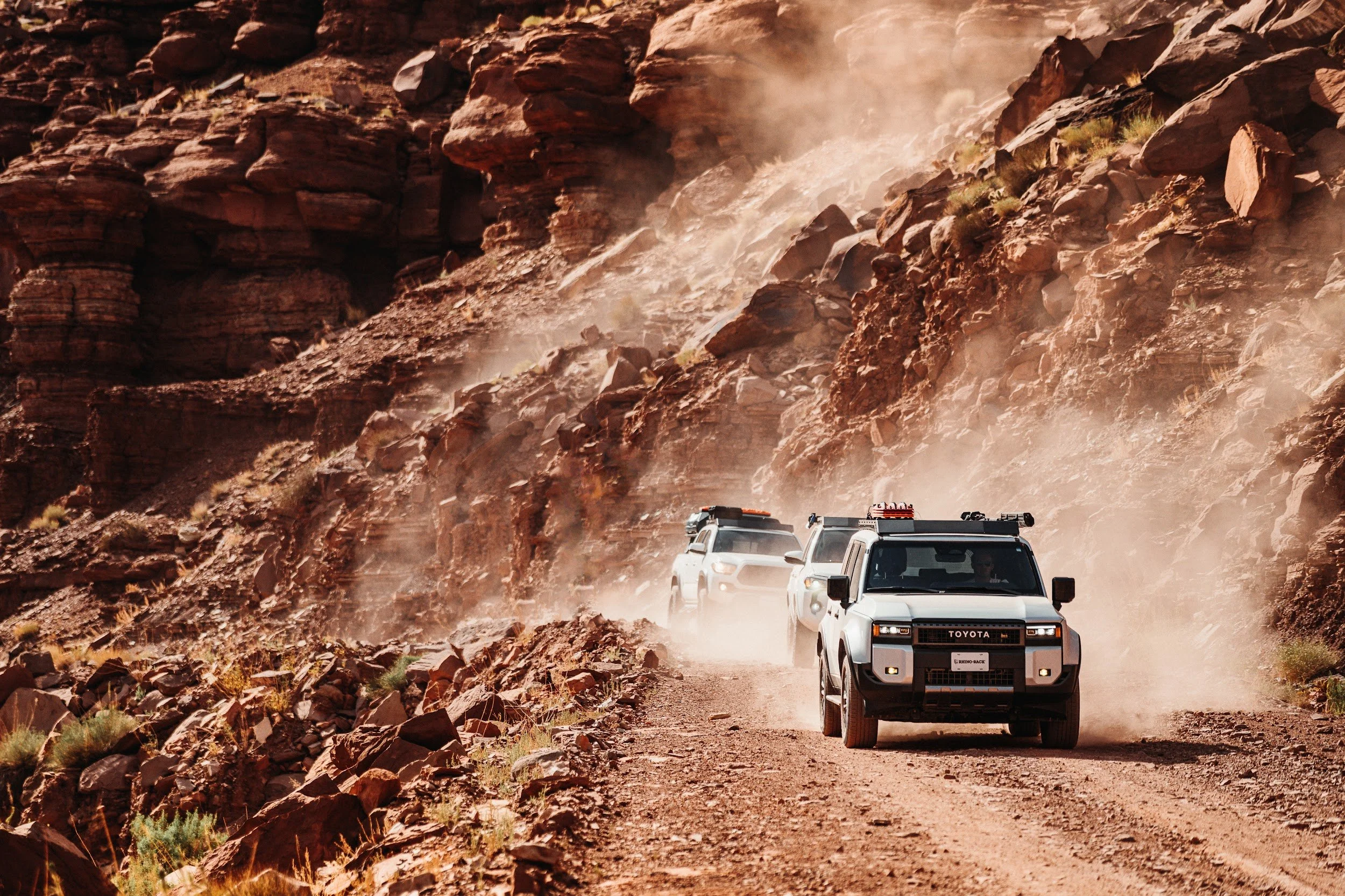 Land Cruiser leading the convoy through a red rock canyon in Utah, dust hanging behind.