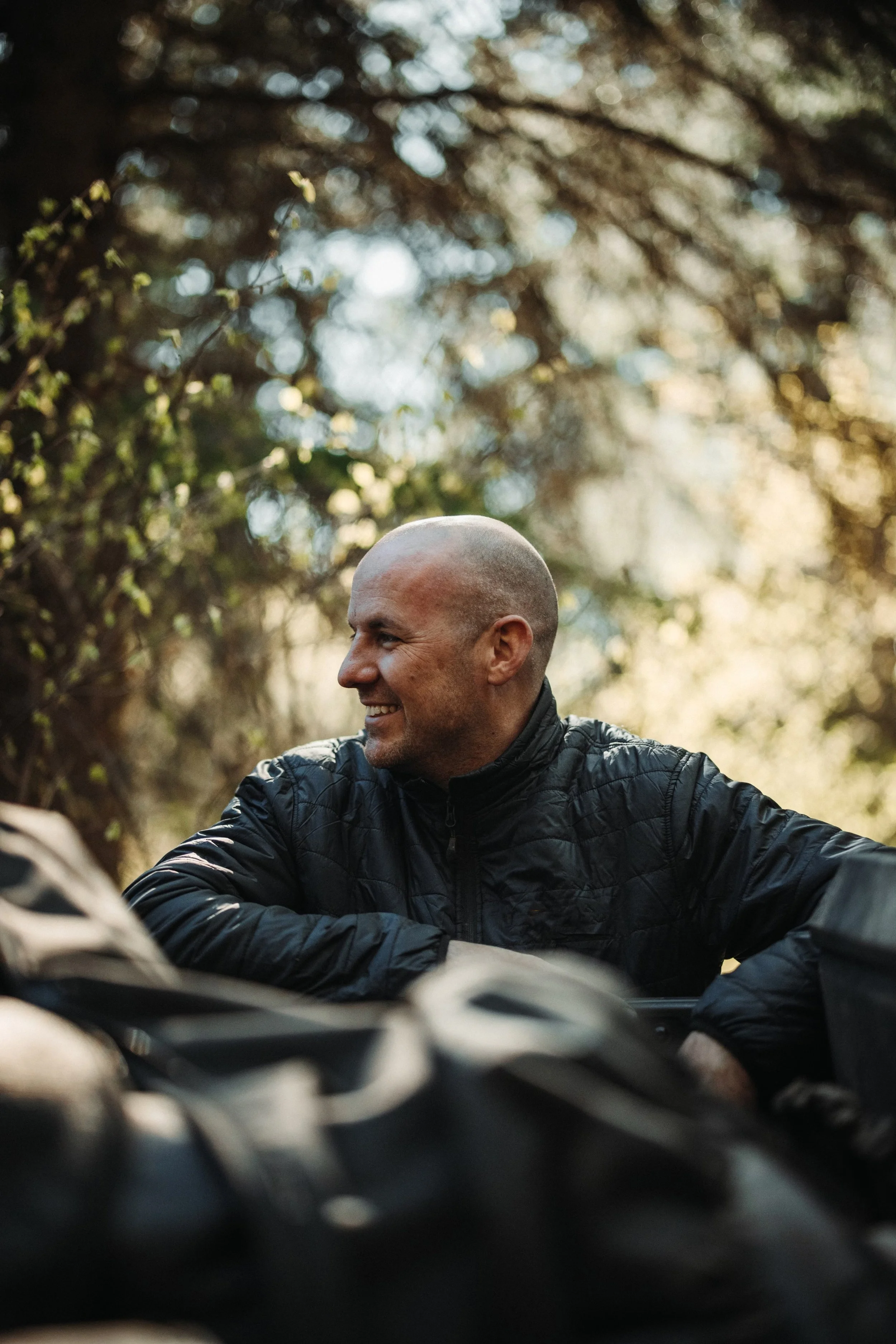 Phil Henderson on location, seated beside a vehicle under the trees