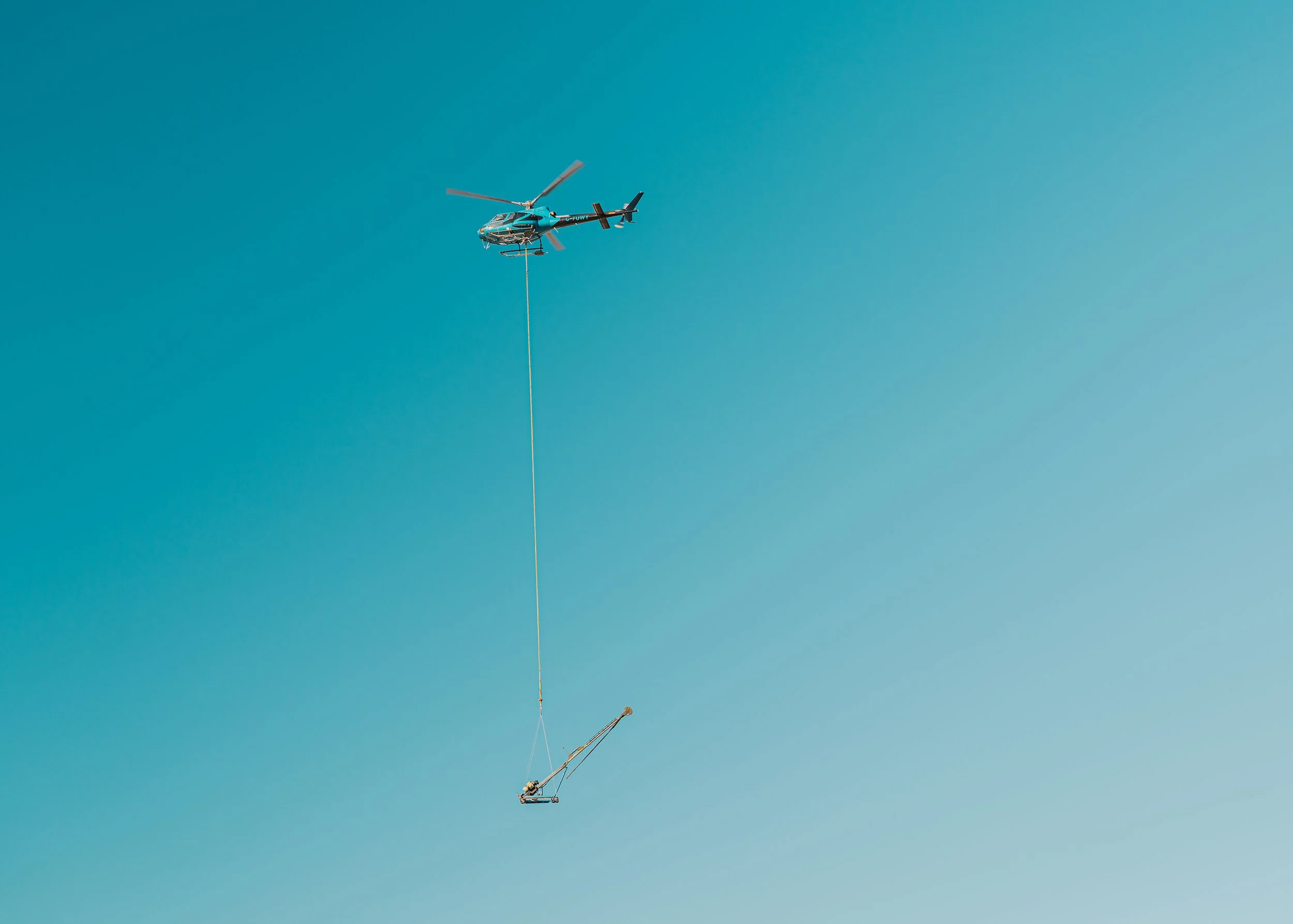 Helicopter carrying a long-line load against a blue sky
