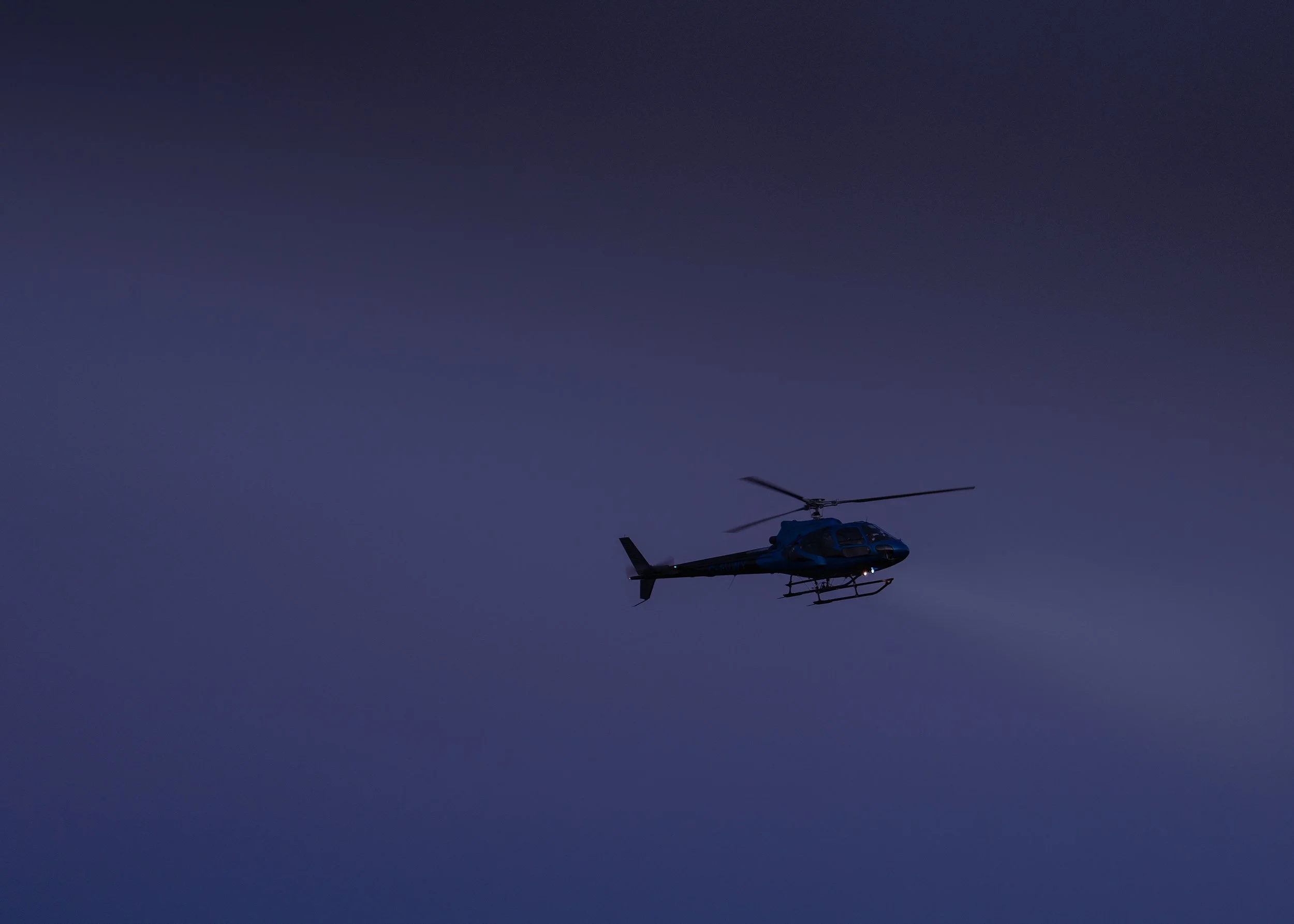 Helicopter silhouetted against a dark blue evening sky
