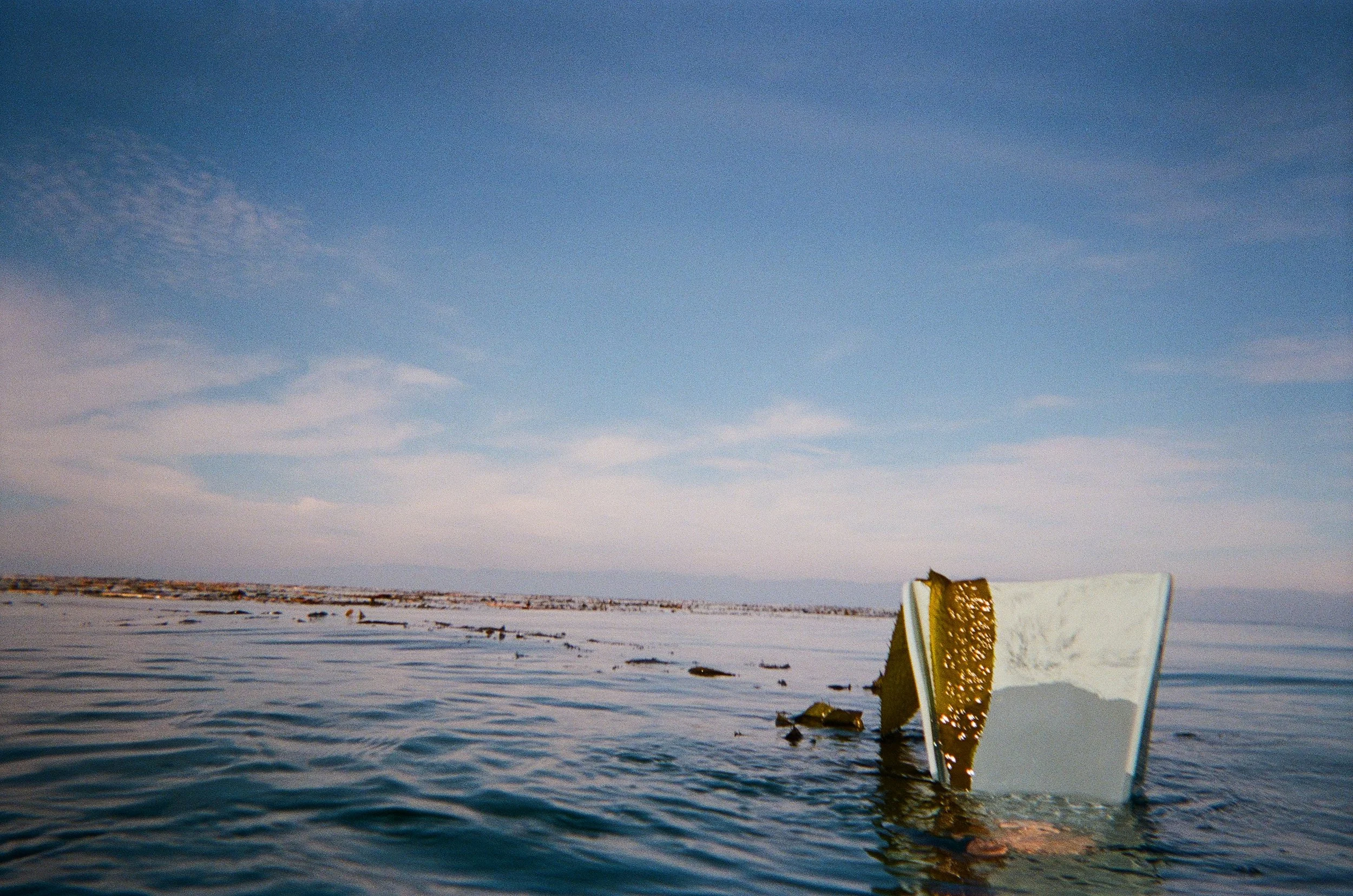 Sailboat submerged in water, with part of the boat visible above the waterline, in a body of water on a clear day with a blue sky.