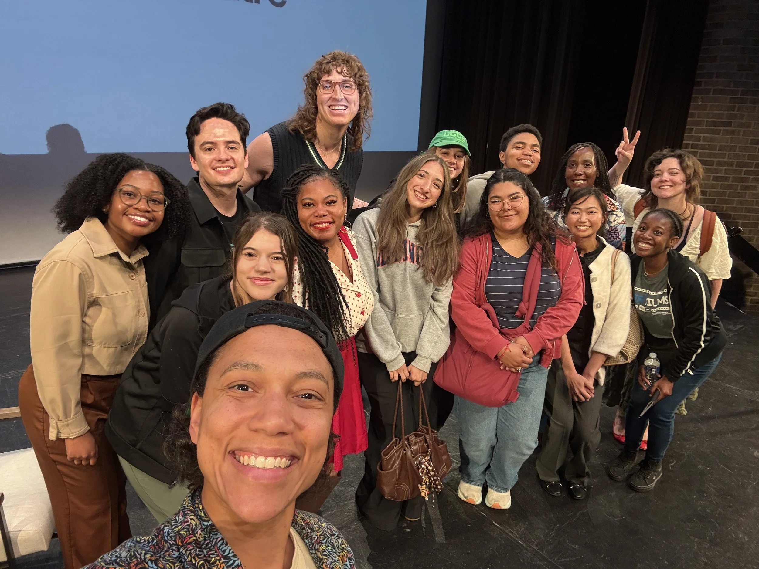 Group of diverse young adults posing together for a photo at an indoor event, smiling and making peace signs.