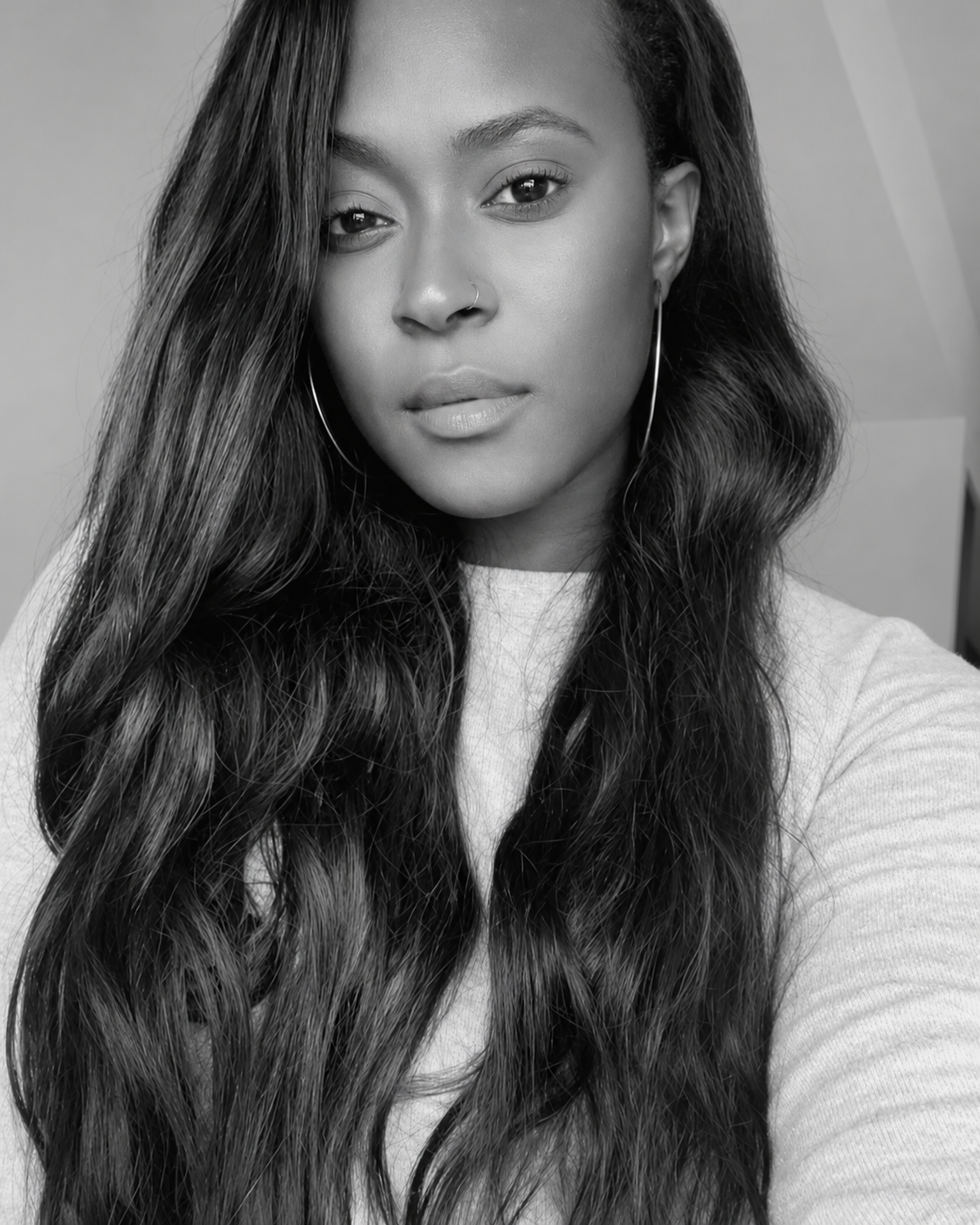 Close-up black-and-white portrait of a young woman with long wavy hair, wearing hoop earrings, and a light top.