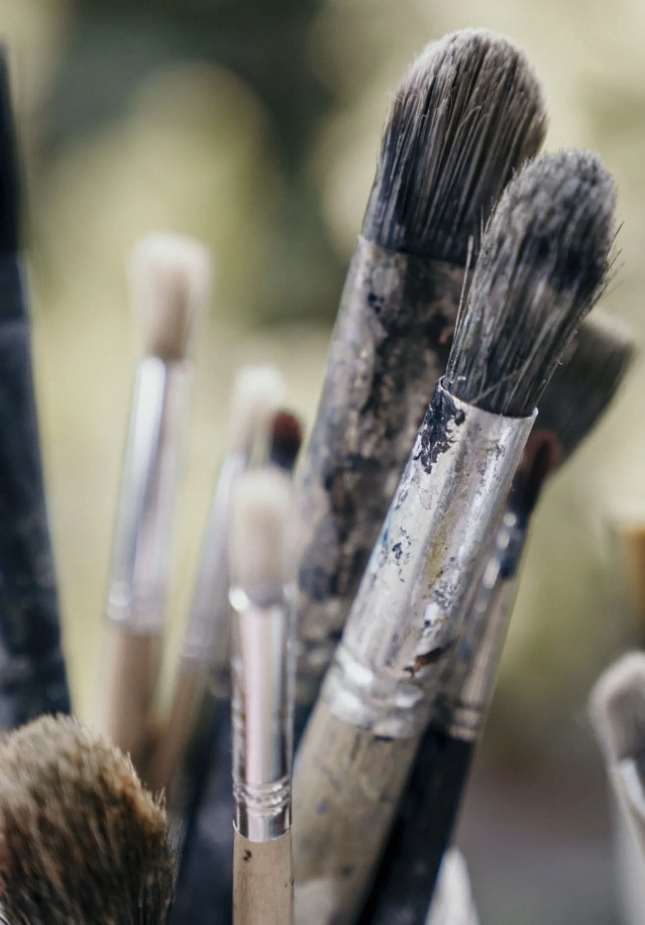Close-up of paintbrushes with weathered bristles, some with paint residue, in a holder.