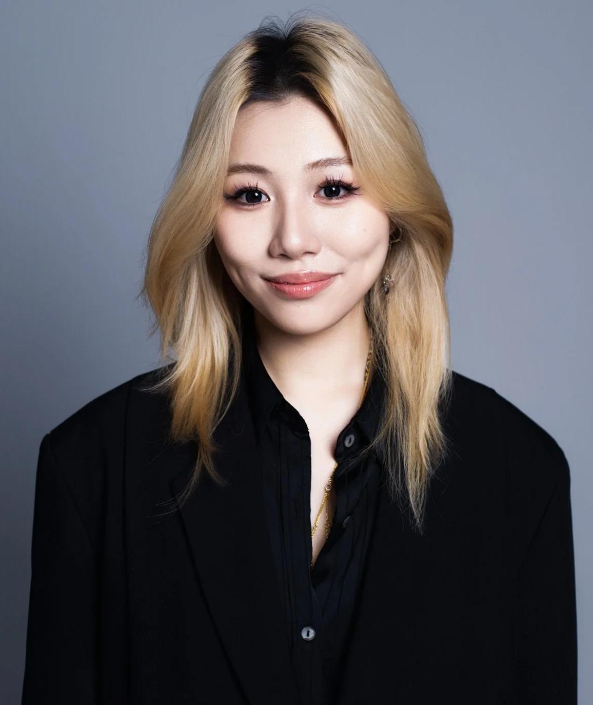 Portrait of a woman with blonde hair, wearing a black shirt, smiling against a gray background.