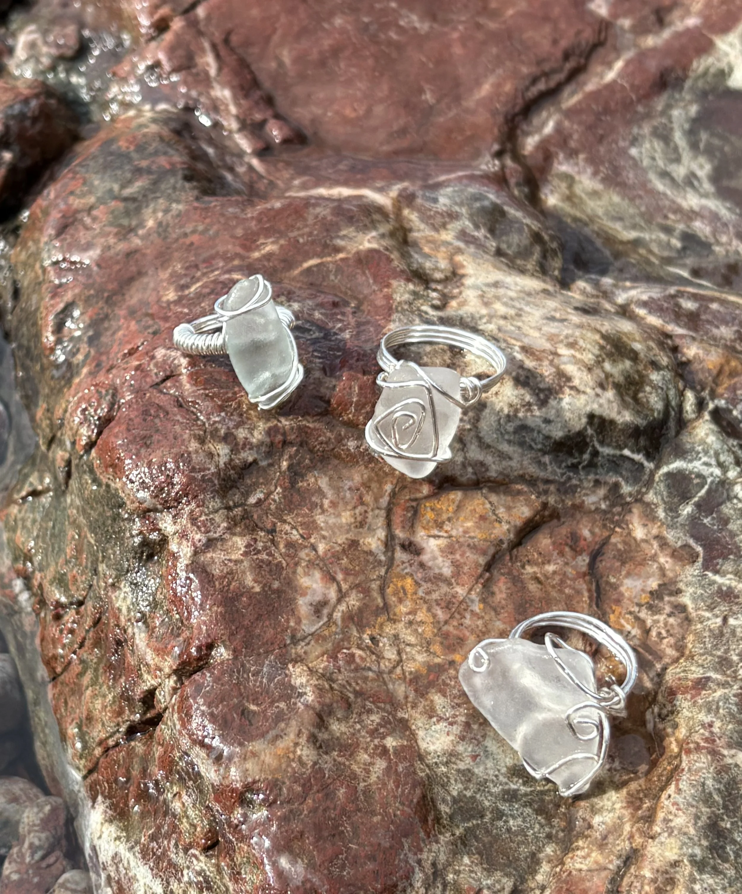 Close-up of a rocky surface with two piece of jewelry, one a ring and the other a necklace, both made of silver with abstract, curved designs.