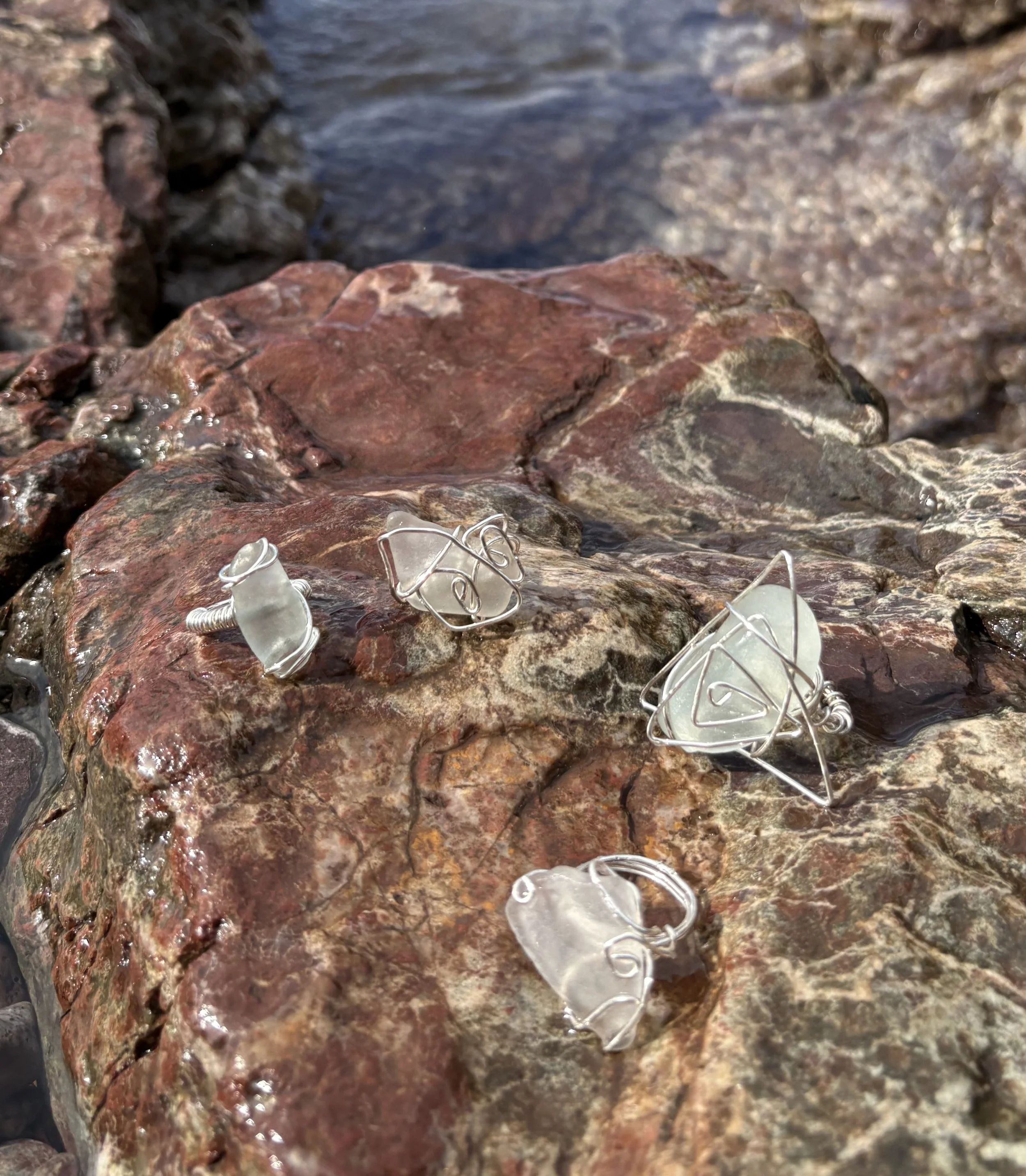 Close-up of wet reddish-brown and gray rocks with some small glass and wire objects on the surface, with water in the background.