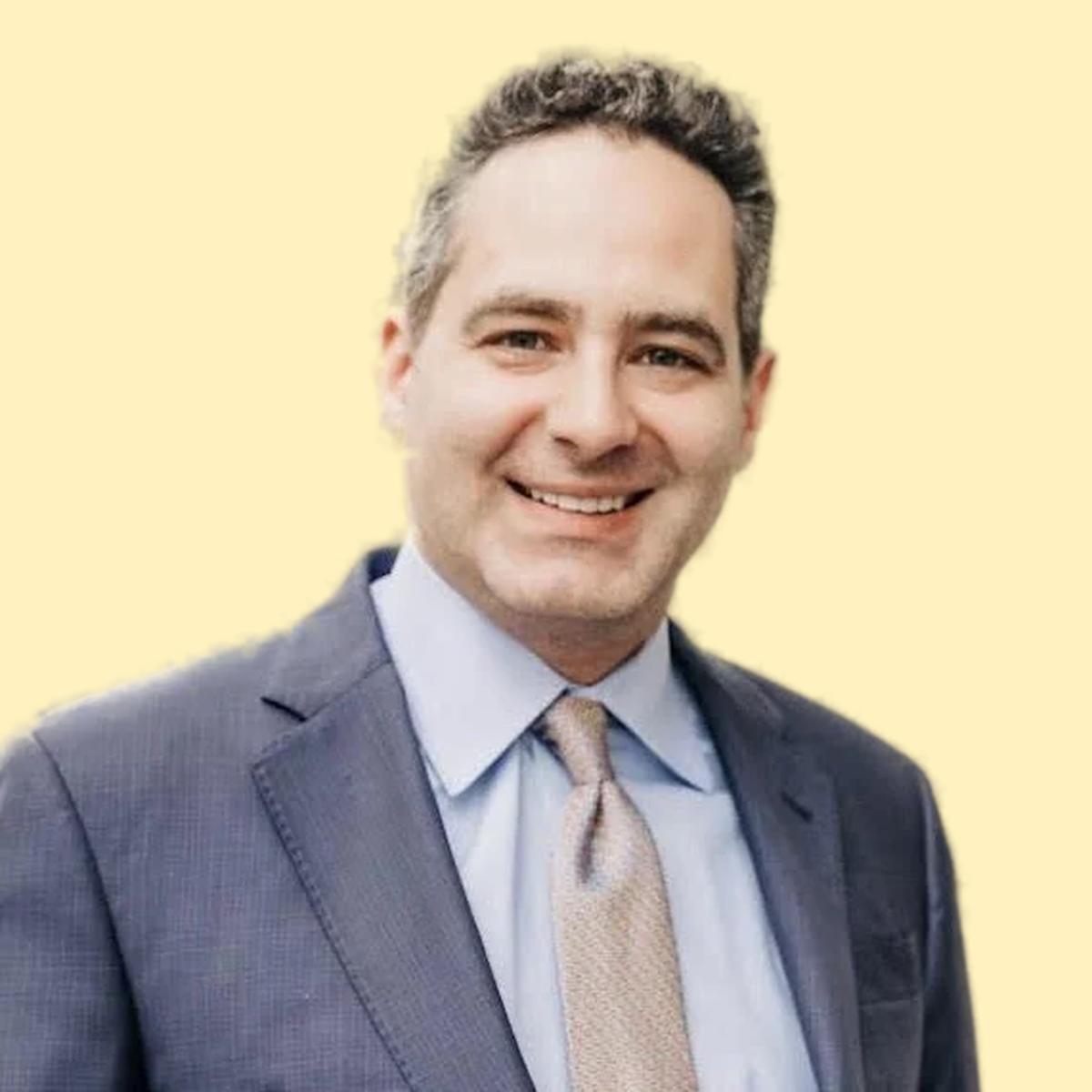 Portrait of a smiling man in a dark suit with a light blue shirt and a beige tie, against a light yellow background.