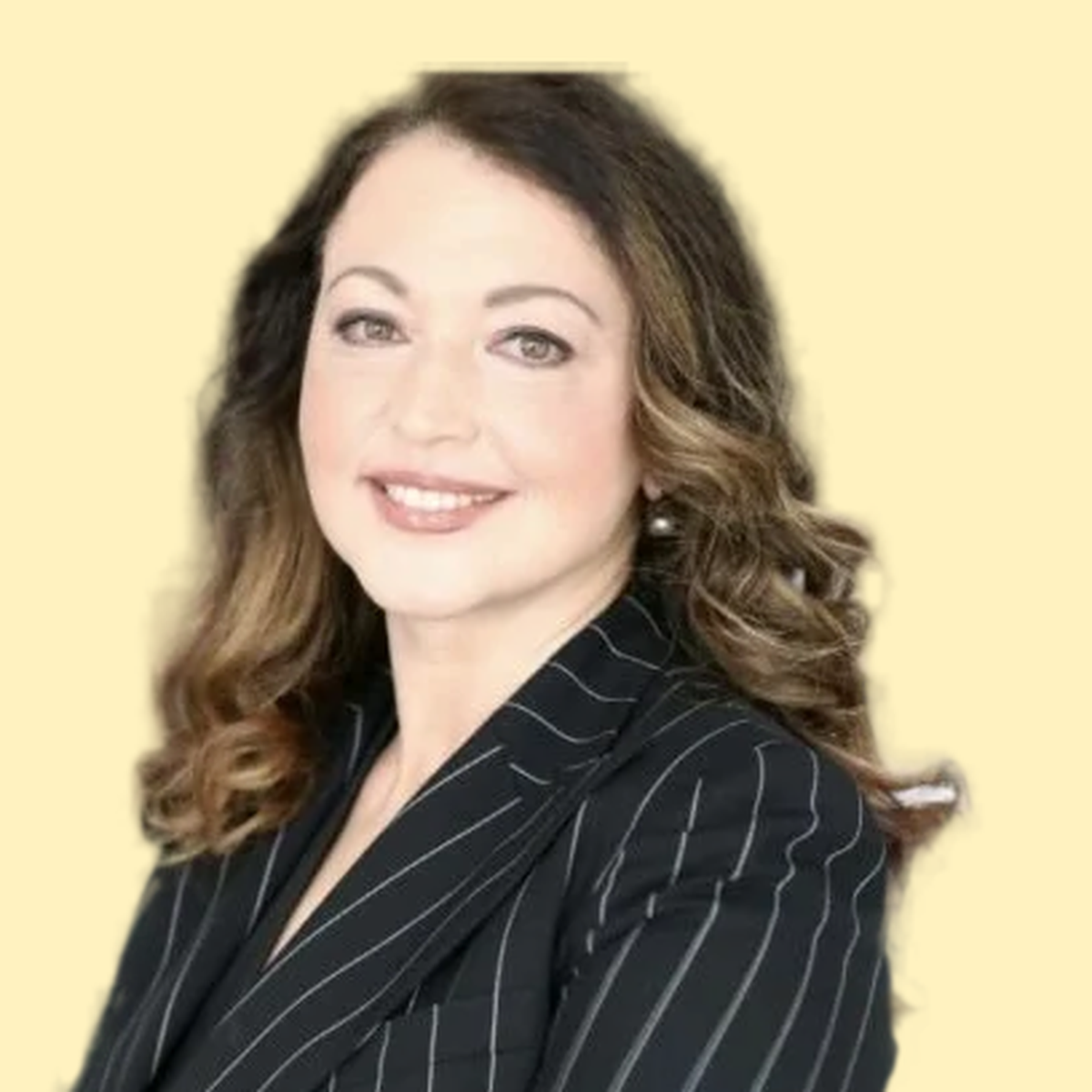 A woman with shoulder-length wavy brown hair with highlights, smiling, wearing a black blazer with white pinstripes, against a light yellow background.