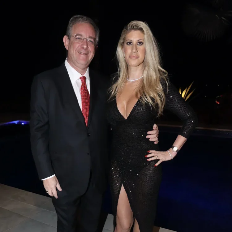 A man and woman dressed in formal evening wear posing together at night, with the woman wearing a black sparkly dress with a deep neckline and high slit, and the man in a black suit with a red tie.