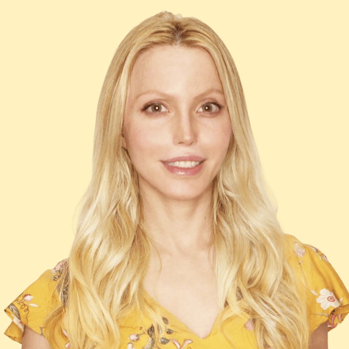 A woman with long blonde hair wearing a yellow floral top, smiling at the camera against a light yellow background.
