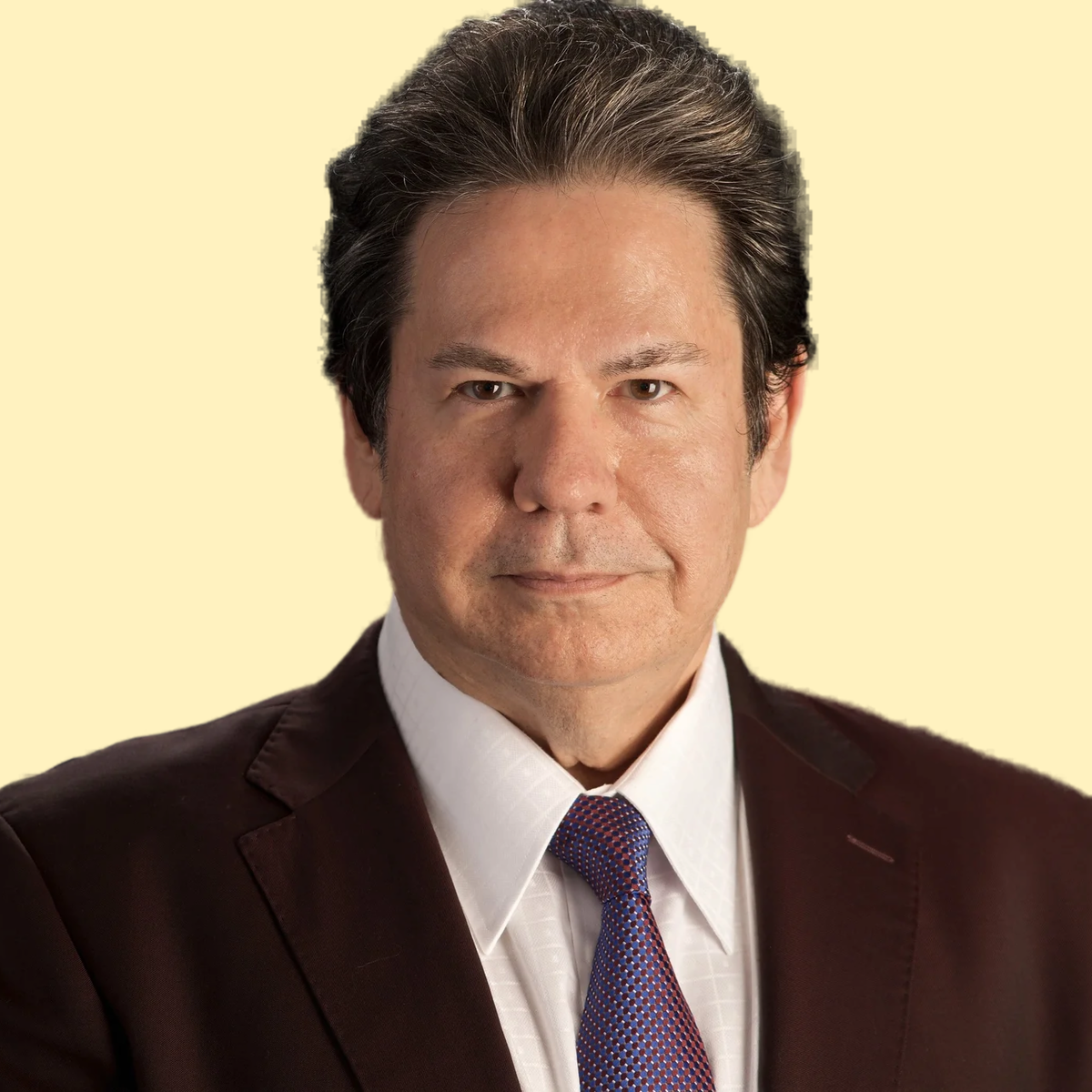 Close-up portrait of a man with dark hair, wearing a suit and tie, against a light yellow background.