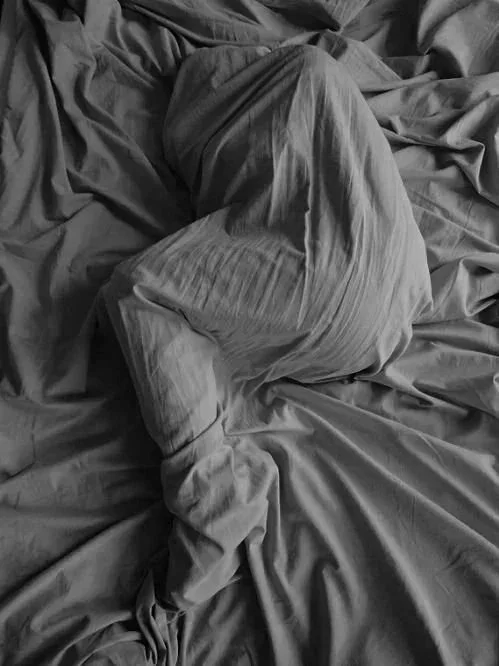 Person curled beneath white sheets on a bed