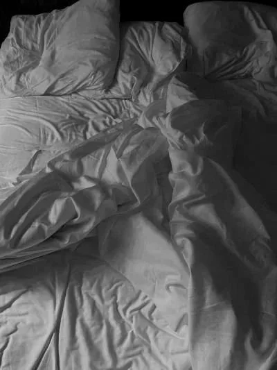 A messy bed with rumpled sheets and pillows.