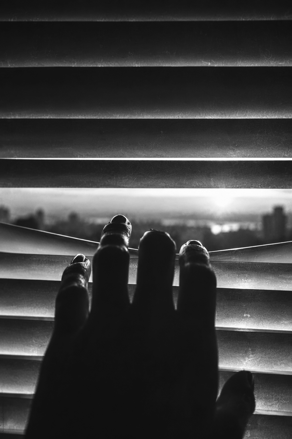 Hand reaching through partially closed window blinds