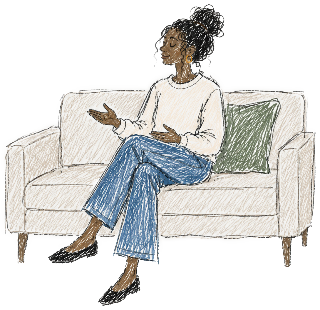 A woman sitting on a beige sofa, gesturing with her hands and speaking, with a green pillow behind her, next to a window with blinds.