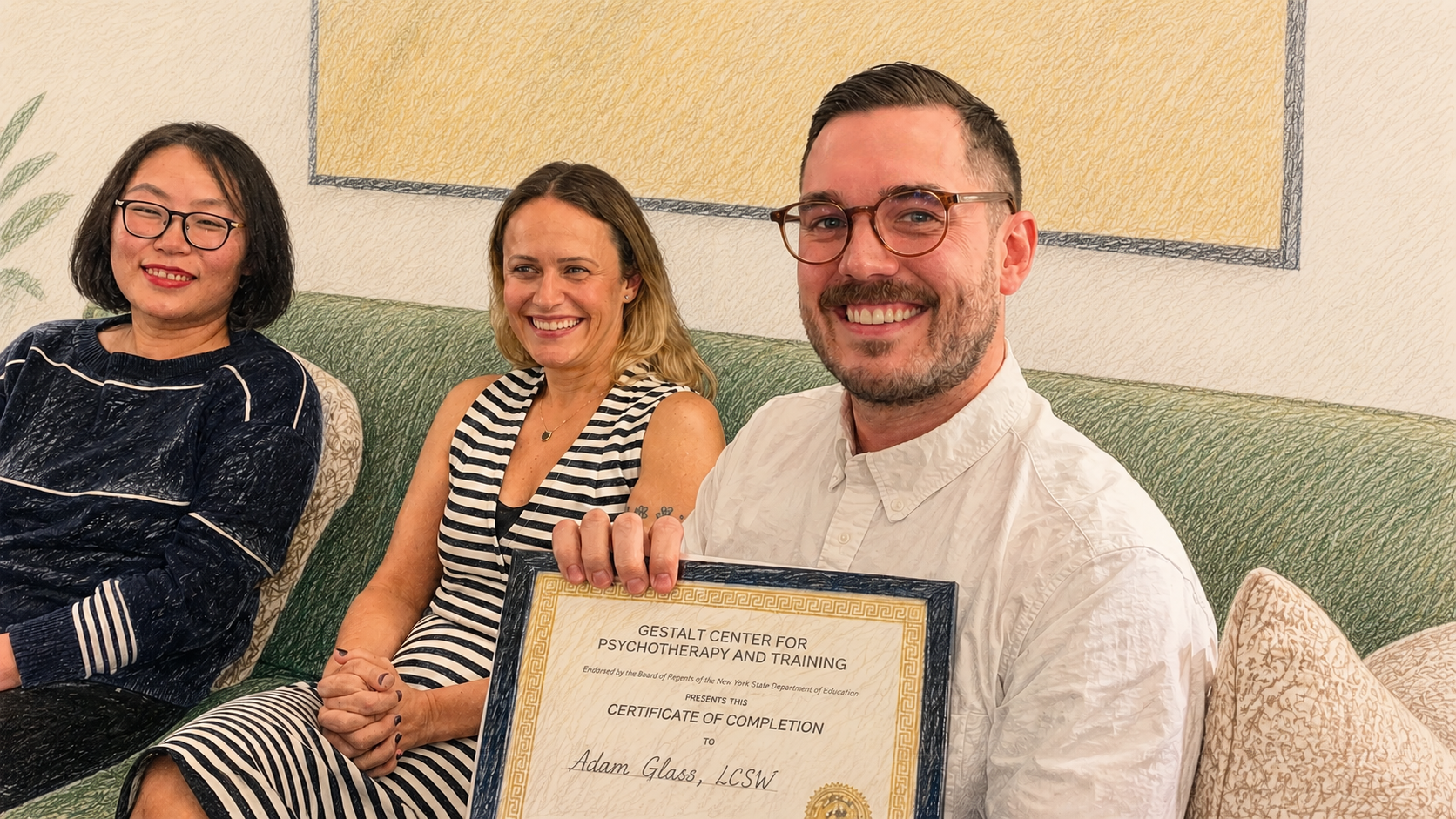 Three smiling people sitting on a green couch, two women and one man holding a framed certificate of completion. The man is wearing glasses and a white shirt, the woman in the middle has shoulder-length blonde hair and is wearing a black and white striped dress, and the woman on the left has short black hair, glasses, and is wearing a dark patterned top.