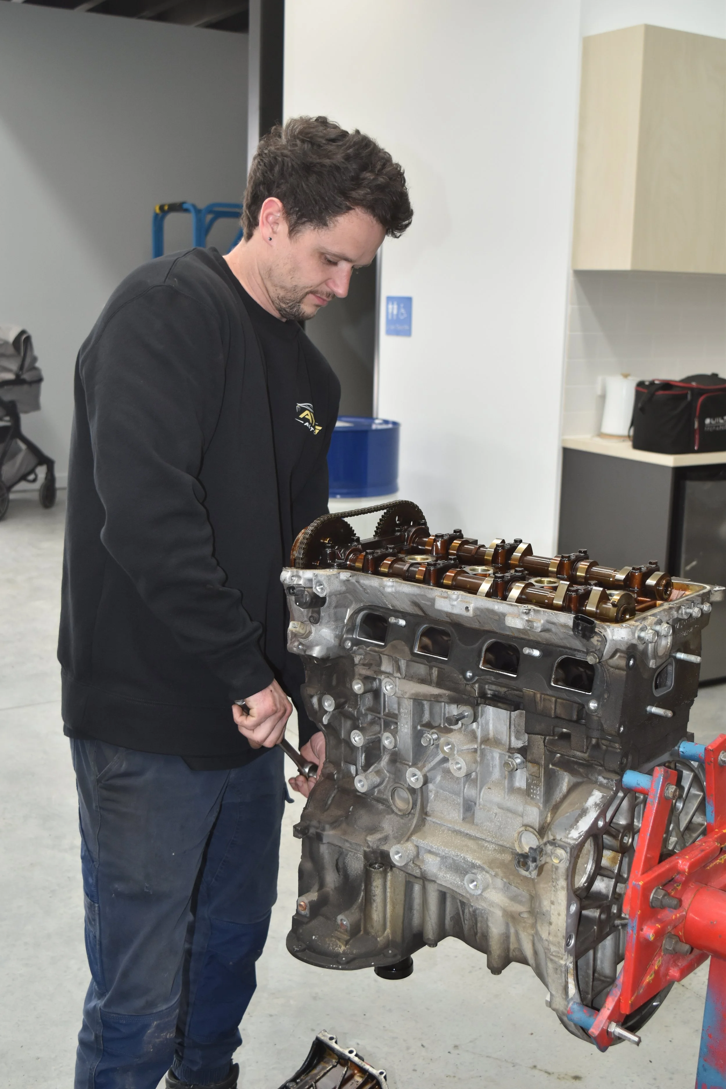 A man working on an engine block, inspecting or assembling it in a workshop or garage setting.
