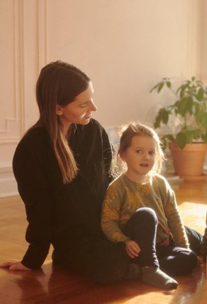 Mother and young daughter sitting together on a sunlit hardwood floor at home