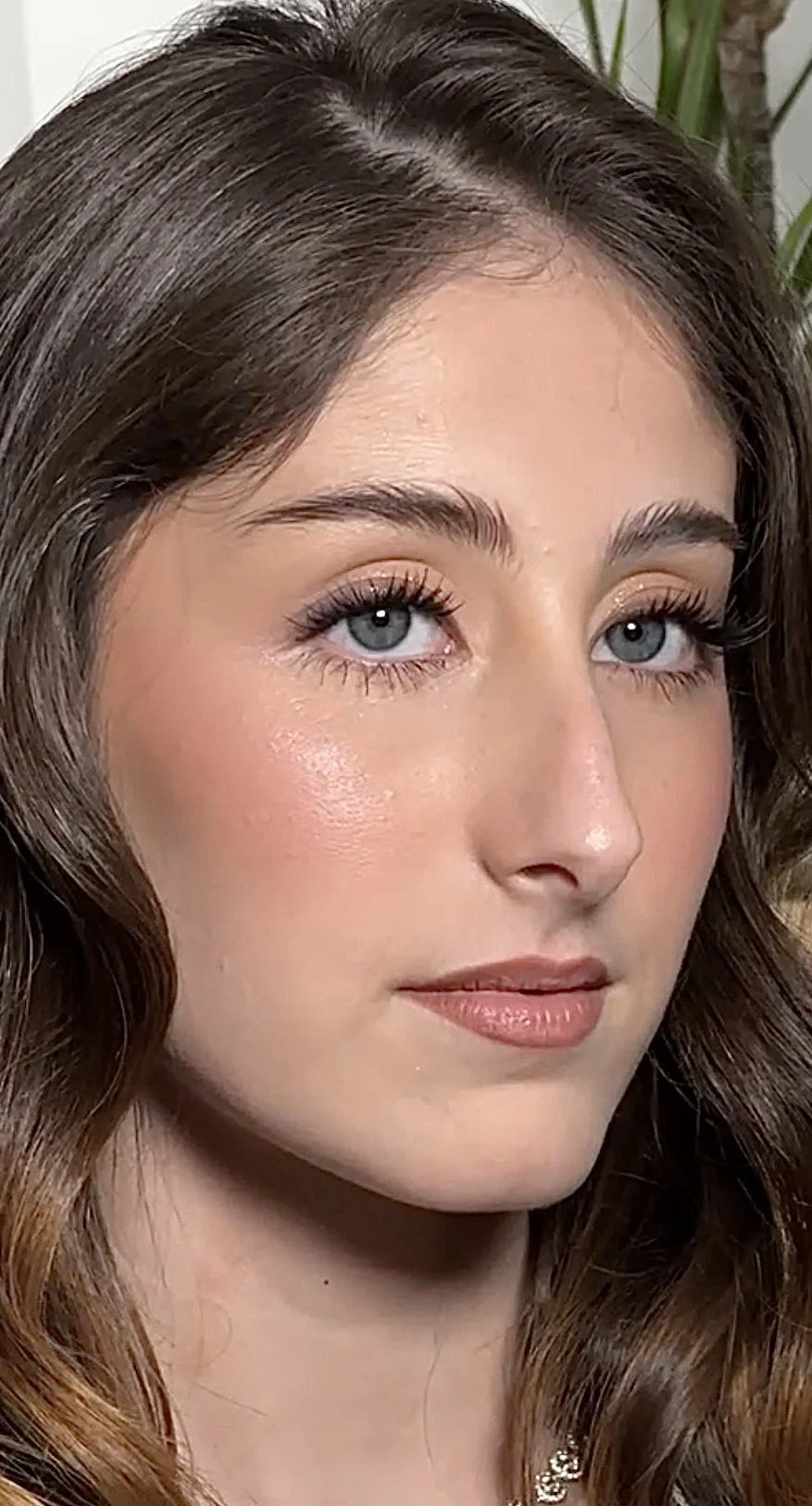 Close-up of a young woman with long, wavy brown hair, blue eyes, and natural makeup.