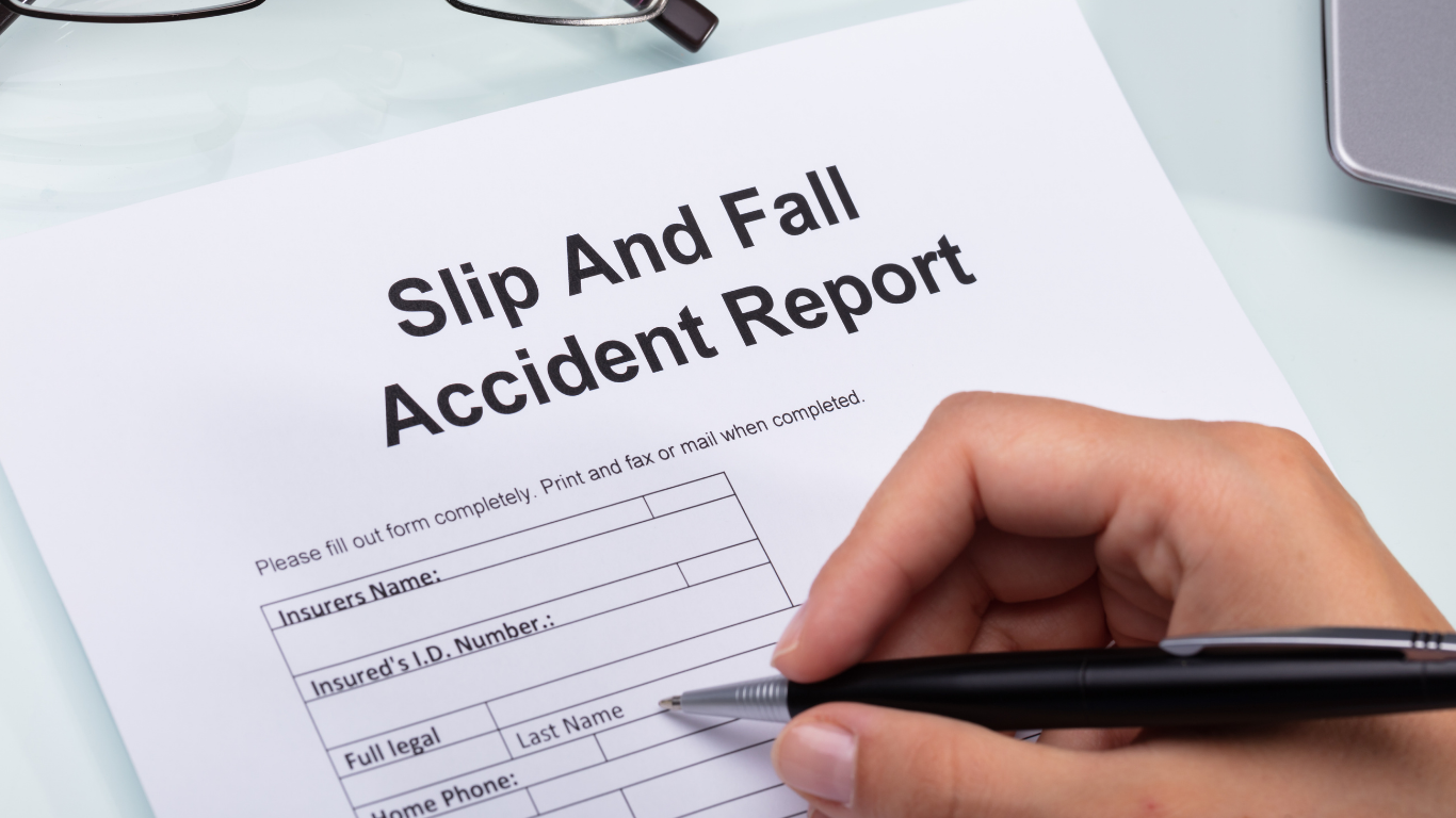 A person filling out a slip and fall accident report form on a desk with a pen in hand.