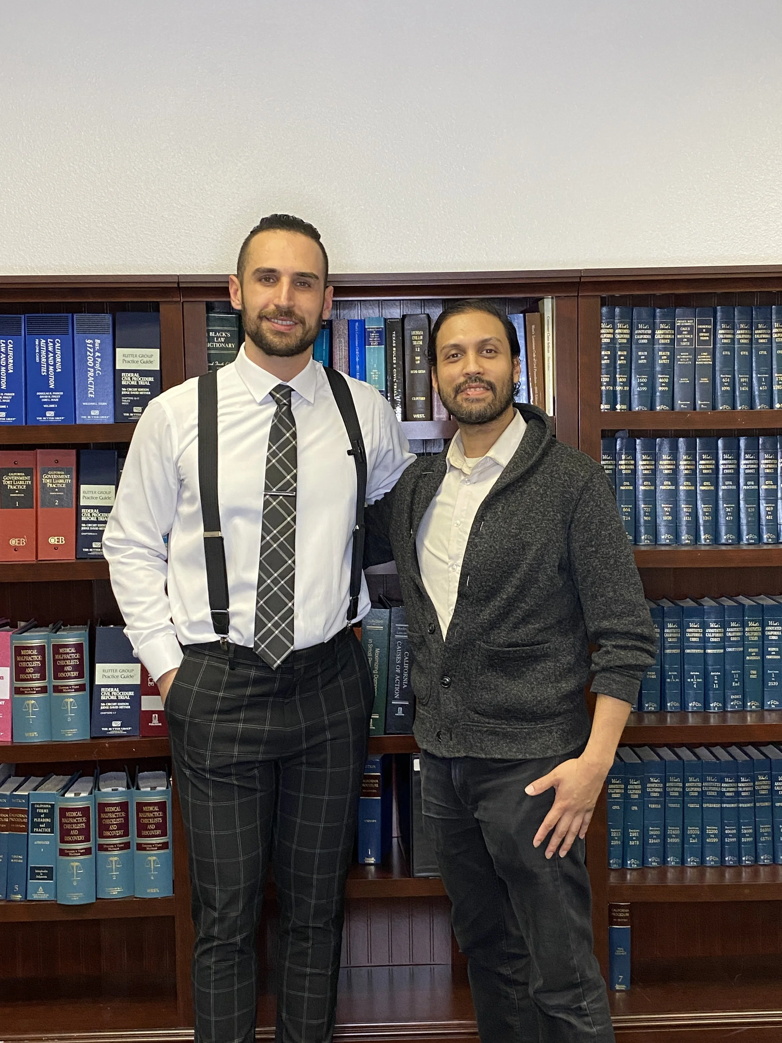Two men standing in front of a bookshelf filled with legal books, dressed in business casual attire.