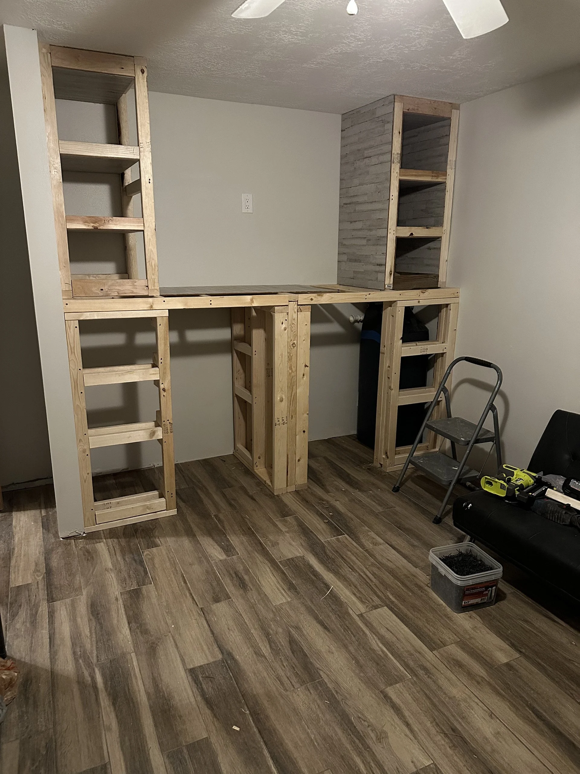 Interior room with partially built wooden shelving and framing, tools on the floor, and a chair.