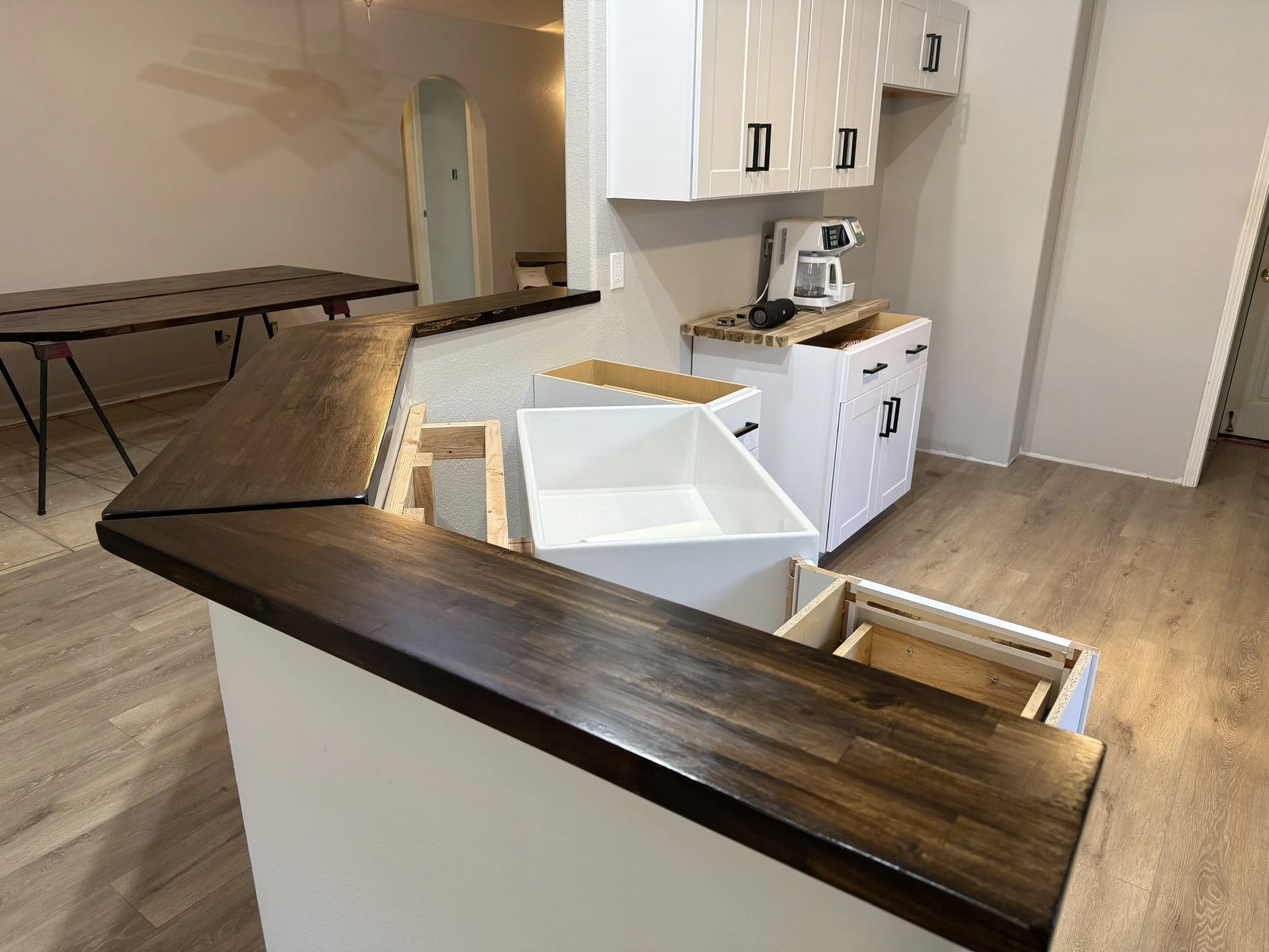 Partially assembled kitchen island with a dark wood top and white base, open drawers, and miscellaneous items on the counter, including a coffee maker, a speaker, and keys.