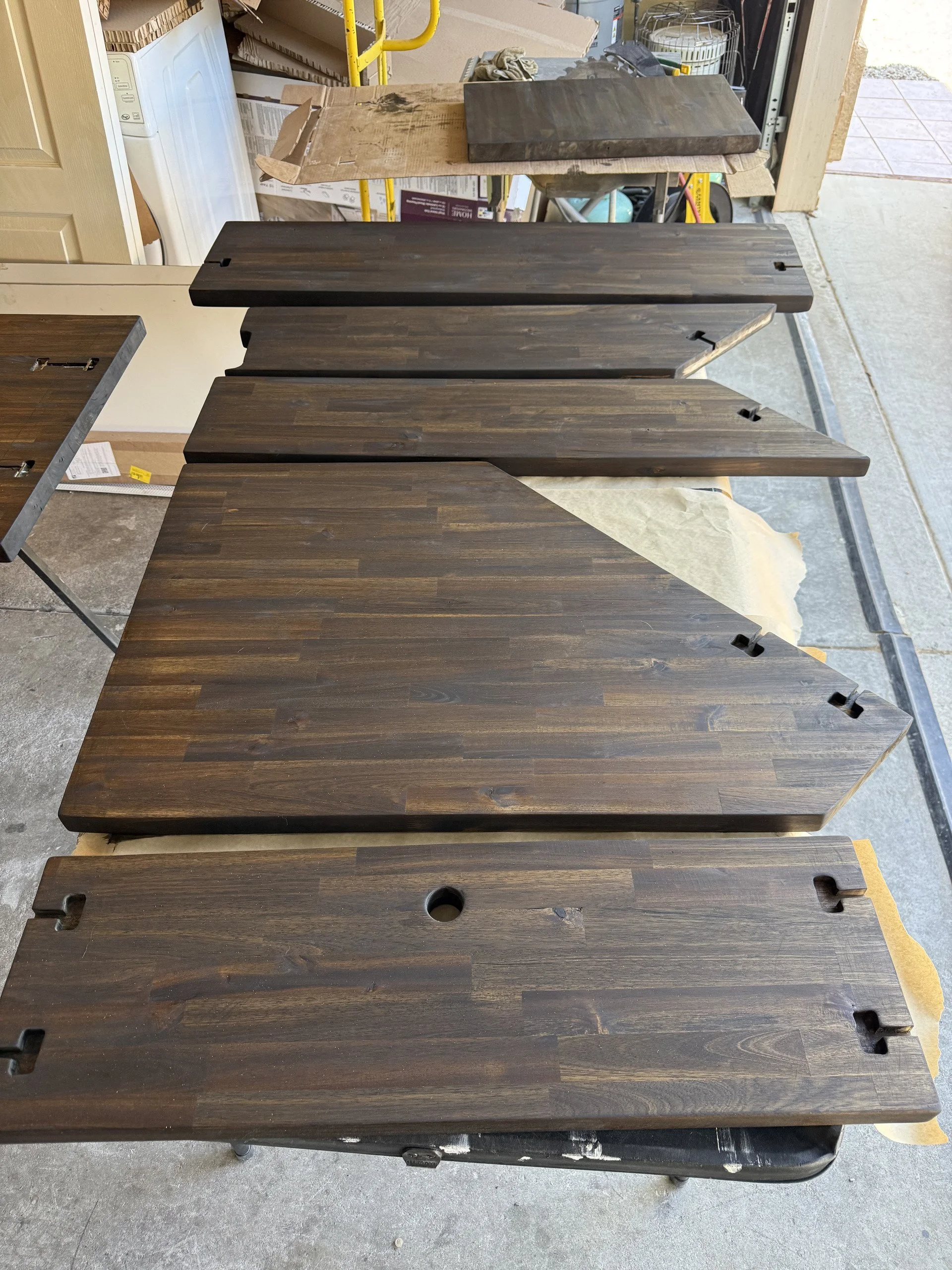 Several dark wooden countertop pieces stacked together in a garage, with a washing machine visible in the background.