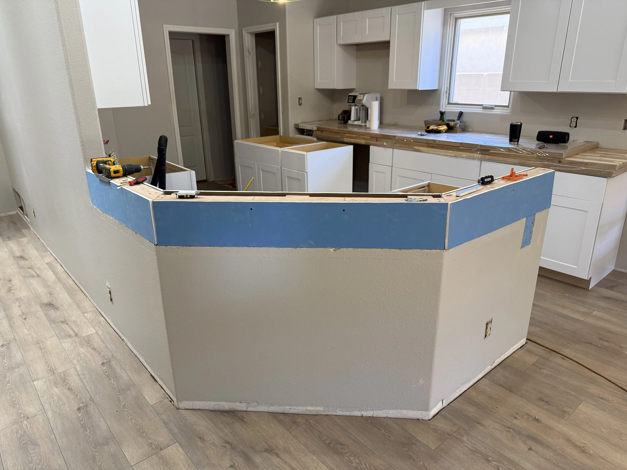 Kitchen under renovation with white cabinets, a window, and a partially built island with tools on top.